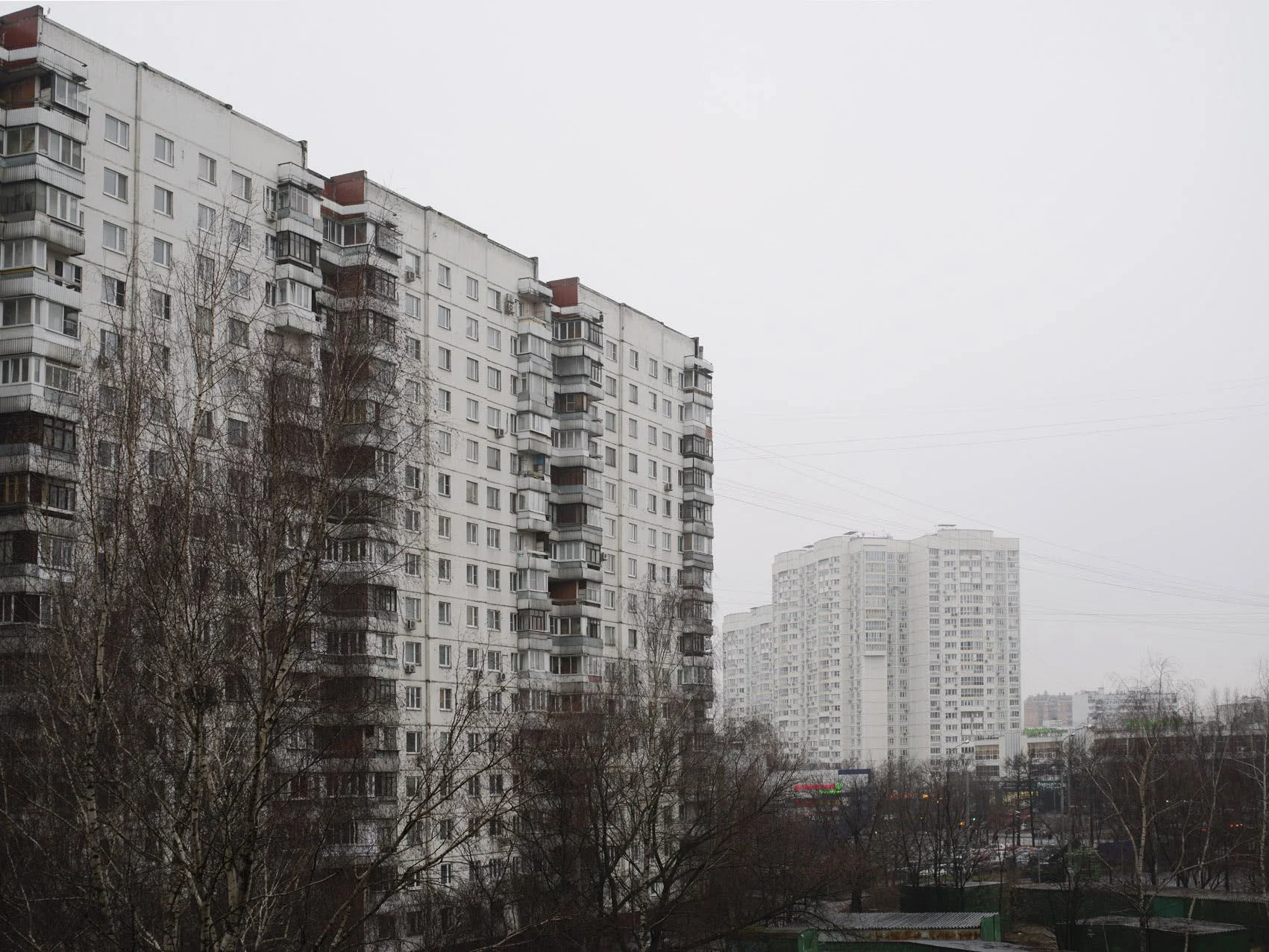 View of multiple tall, white residential apartment buildings on a cloudy, overcast day, with leafless trees in the foreground.