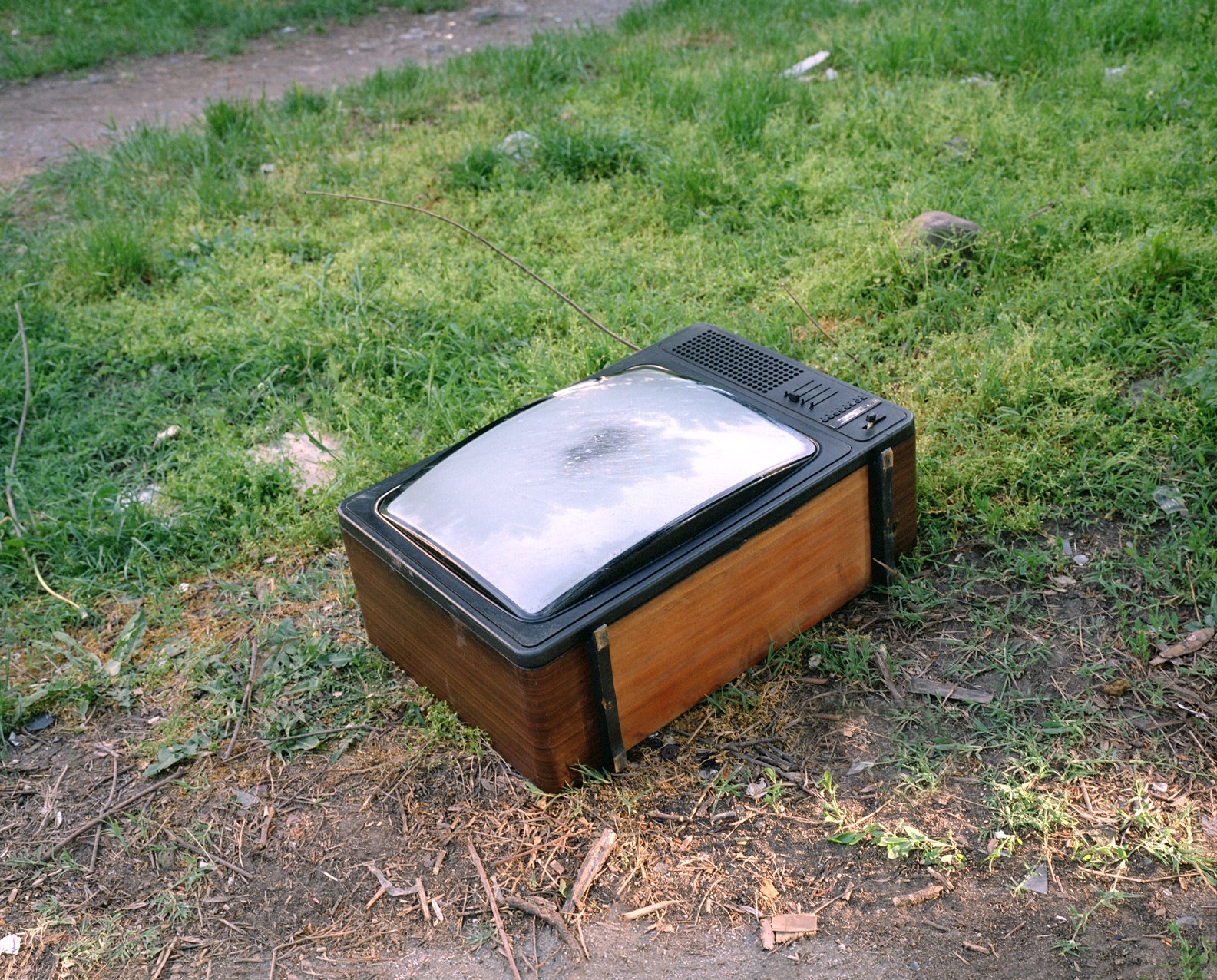 An old-fashioned television set with a wooden exterior and a curved glass screen resting on the grass outdoors.
