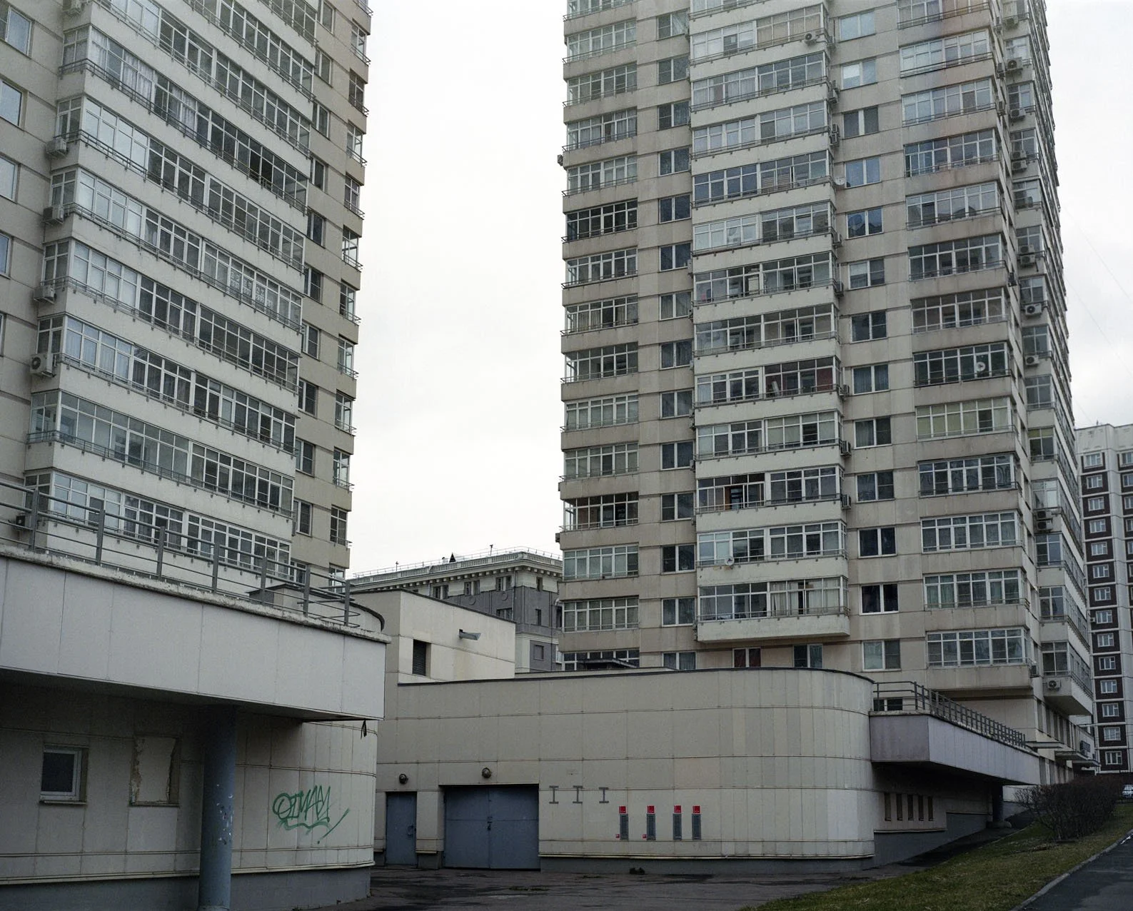 Two tall residential apartment buildings with numerous balconies and many windows, with a lower, curved structure in front.