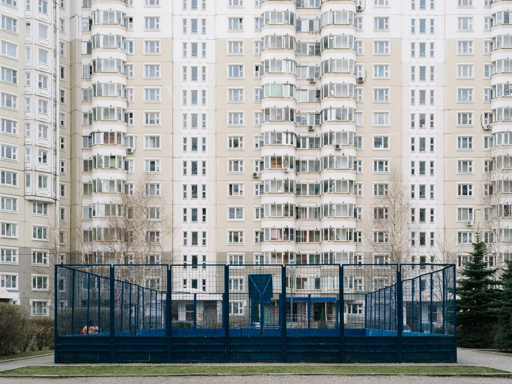 An outdoor sports court with a blue fence in front of a tall, beige residential apartment building.