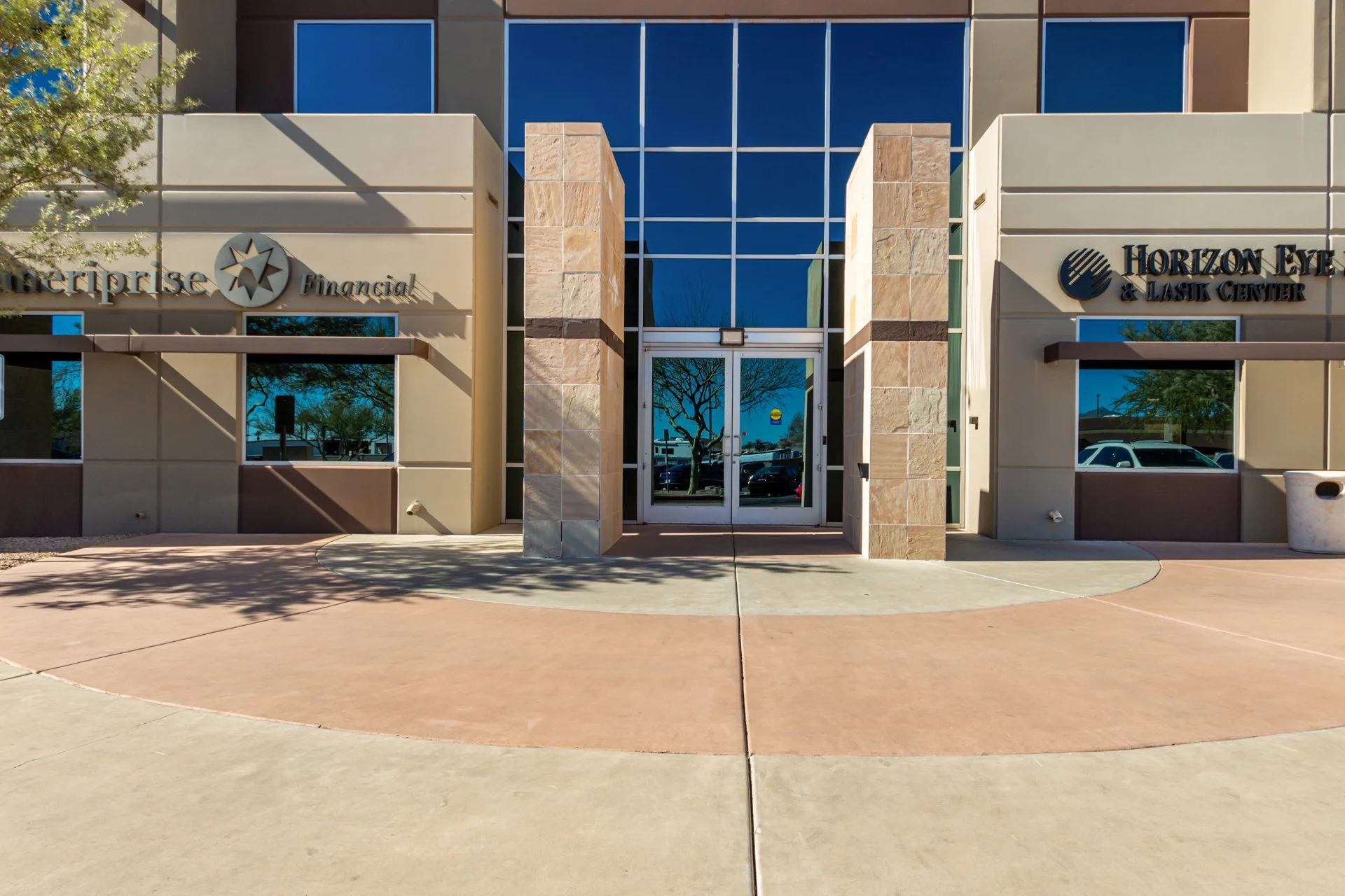 A building glass door entry with surrounding glass reflecting a blue sky with color tones of cream and brown.