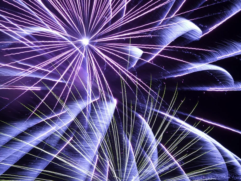 Bright purple and white fireworks exploding in the night sky with streaks of light radiating outward.