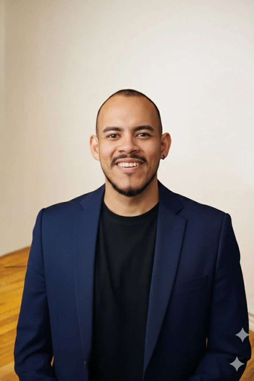 Porträt eines lächelnden Mannes mit dunklem Haar, Bart und Ohrring, in dunklem Hemd und Blazer, vor hellem Hintergrund.