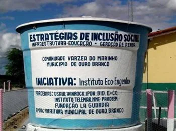 Signboard showing community project details in Portuguese, with the title 'Estratégias de Inclusão Social' and information about a federal initiative.