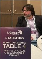 Man with glasses and beard sitting at table with purple sign for IJGlobal and I LATAM 2025 conference, talking at a roundtable on green and sustainable finance.