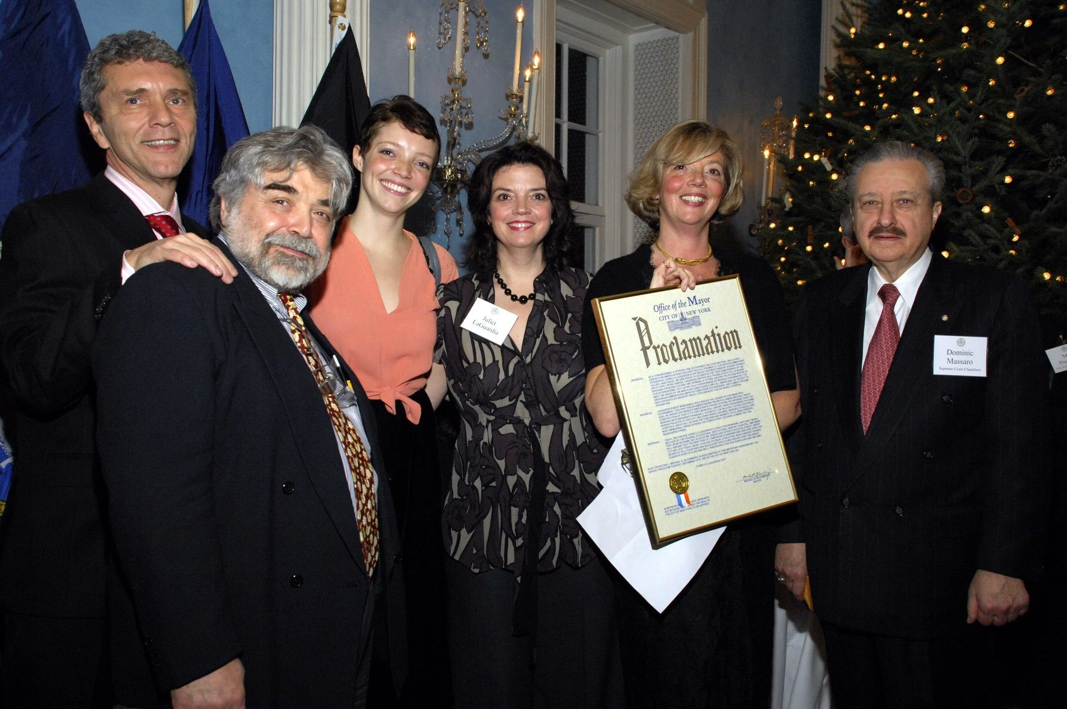Group of people at a holiday party, with Christmas tree, holding a proclamation and smiling for the camera.