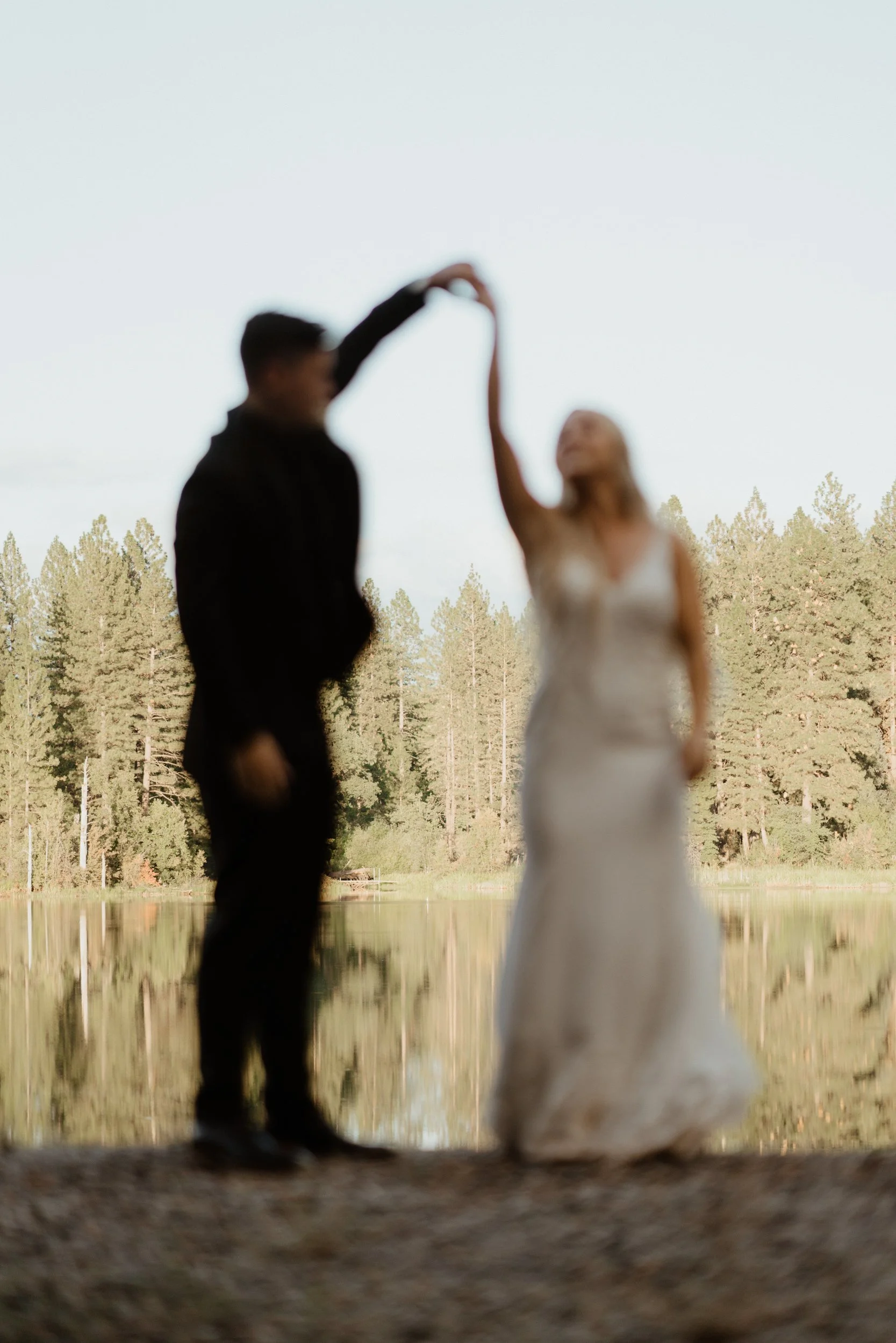 A blurry photo of a couple dancing outdoors near a lake, with trees in the background.
