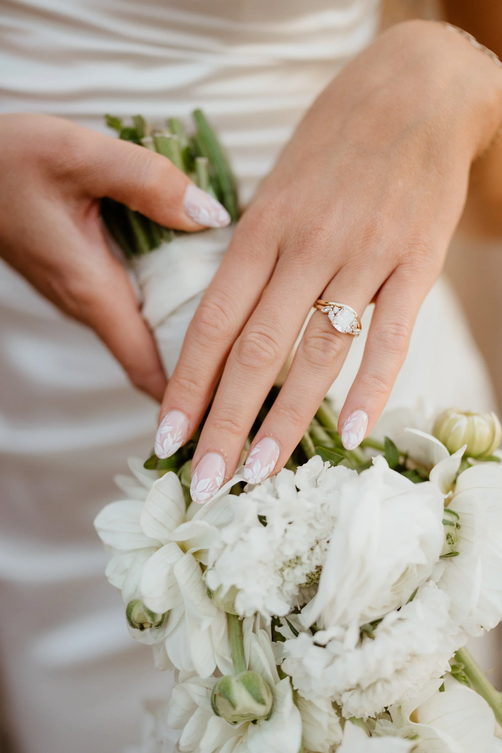 A woman's hand with a wedding ring, placed on a bouquet of white flowers.