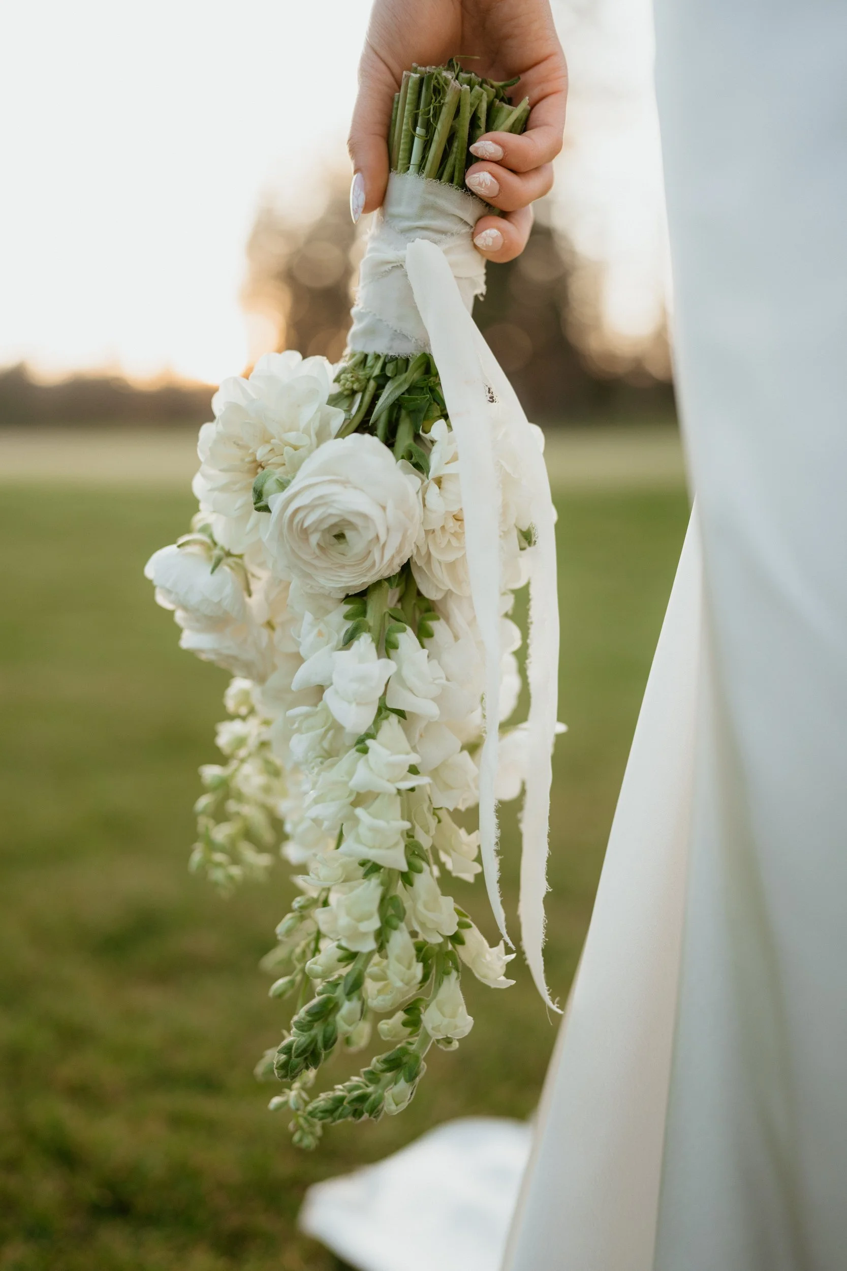 Person holding a cascading white floral bouquet.