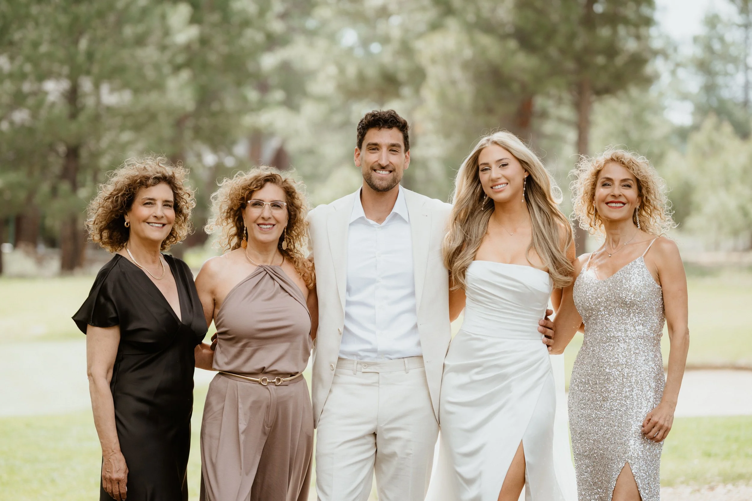 Group of five people standing outdoors in a park, dressed in formal attire, smiling at the camera.