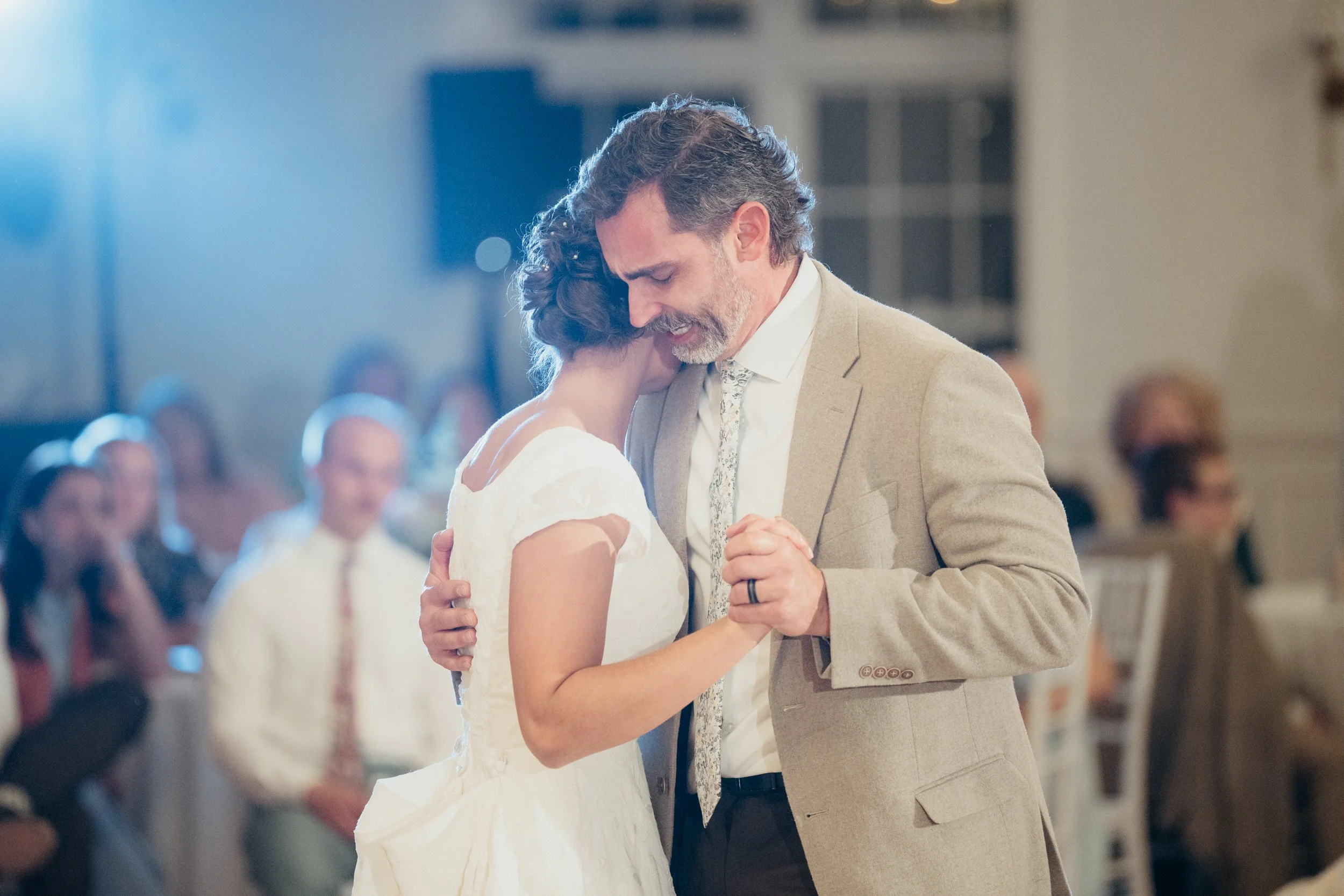 A man and woman dancing closely at a wedding reception, with guests seated in the background.