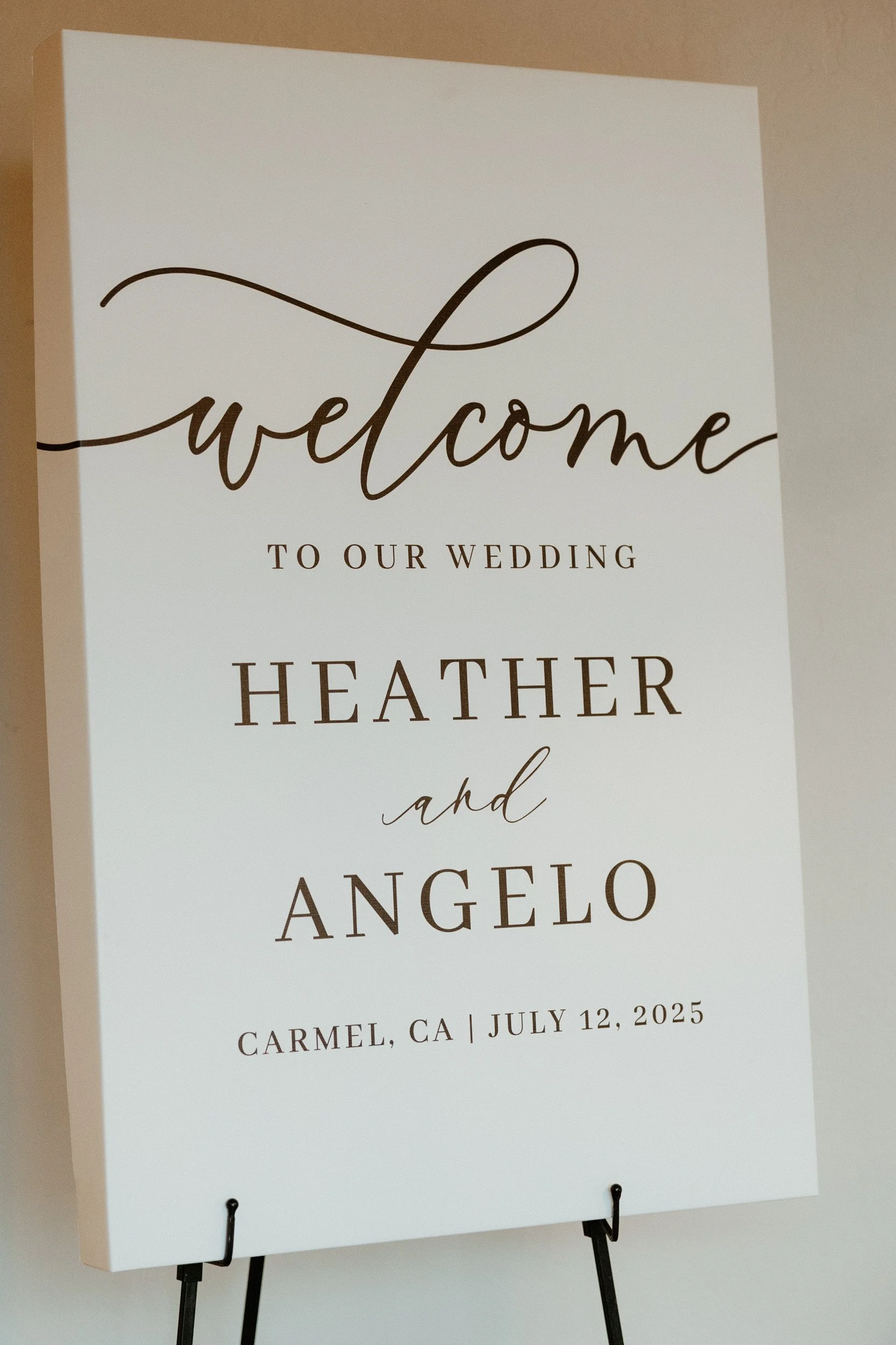 Wedding welcome sign with black text on a white background, displaying the names Heather and Angelo, the date July 12, 2025, and location Carmel, CA.