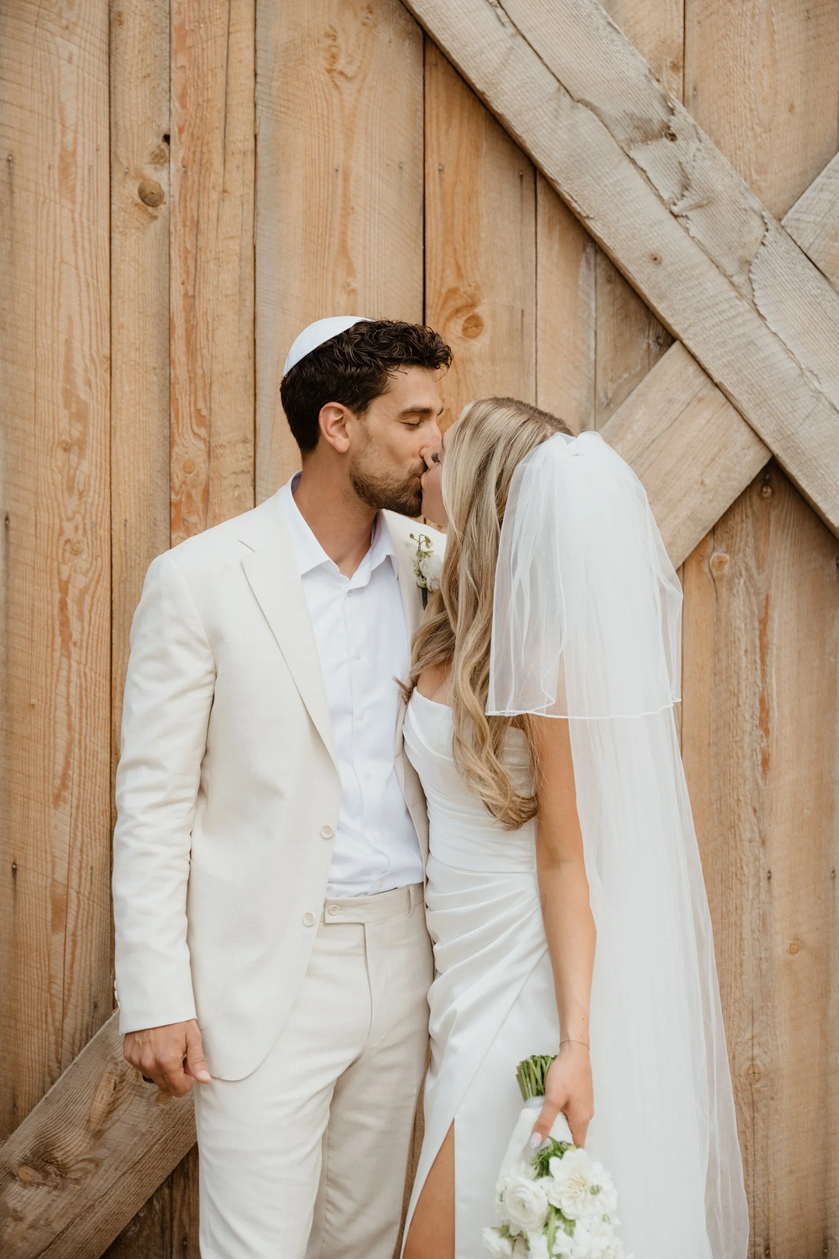 A bride and groom sharing a kiss in front of a rustic wooden barn door.