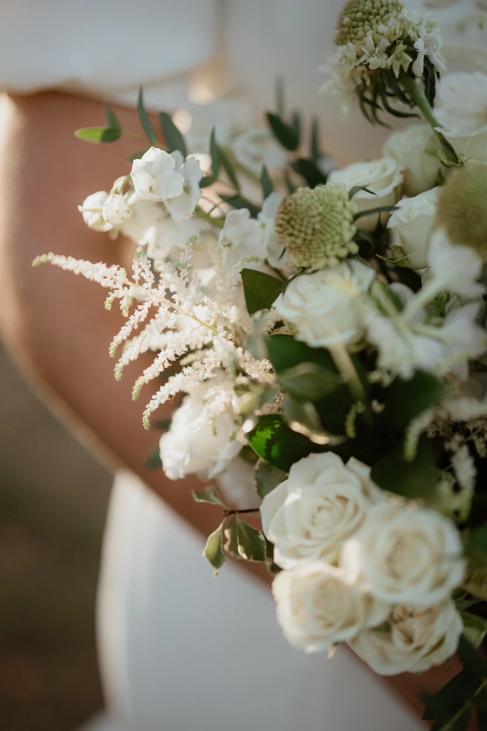 Close-up of a bridal bouquet with white roses, white snapdragons, and various green foliage.