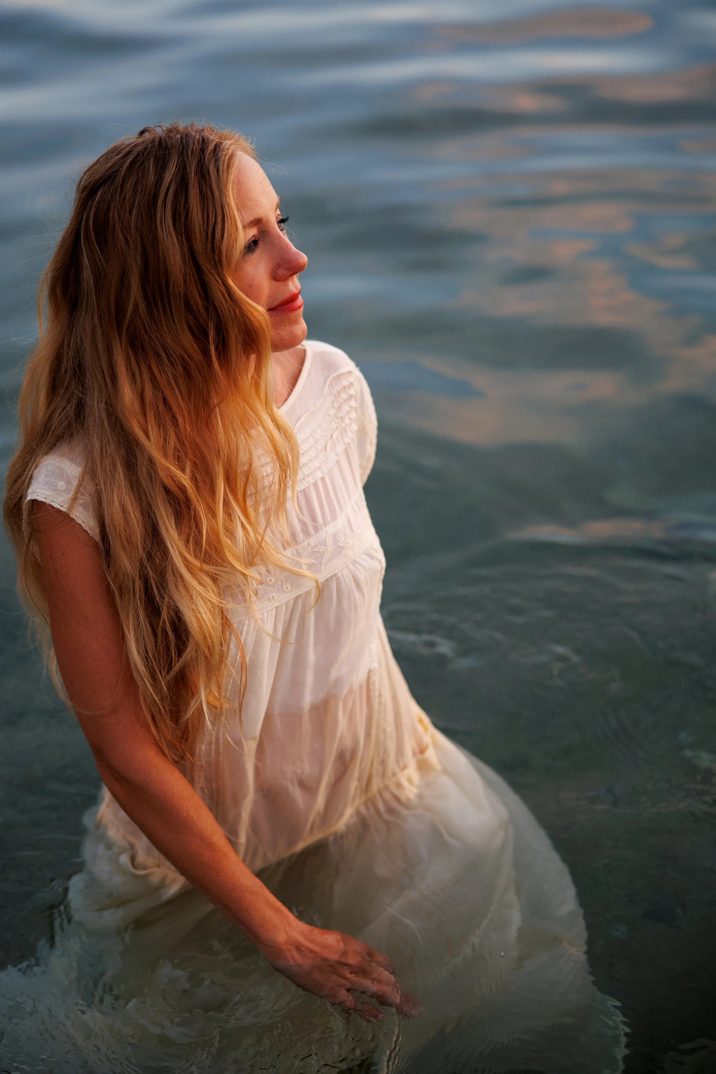 A woman with long red hair in a white dress standing in water