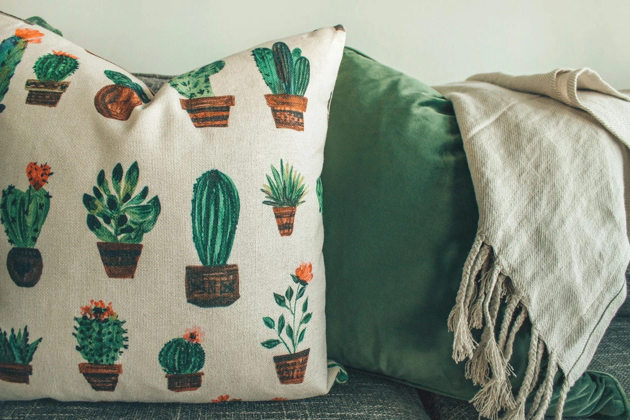 Decorative pillows, one with cactus patterns, and a beige throw blanket on a green sofa.