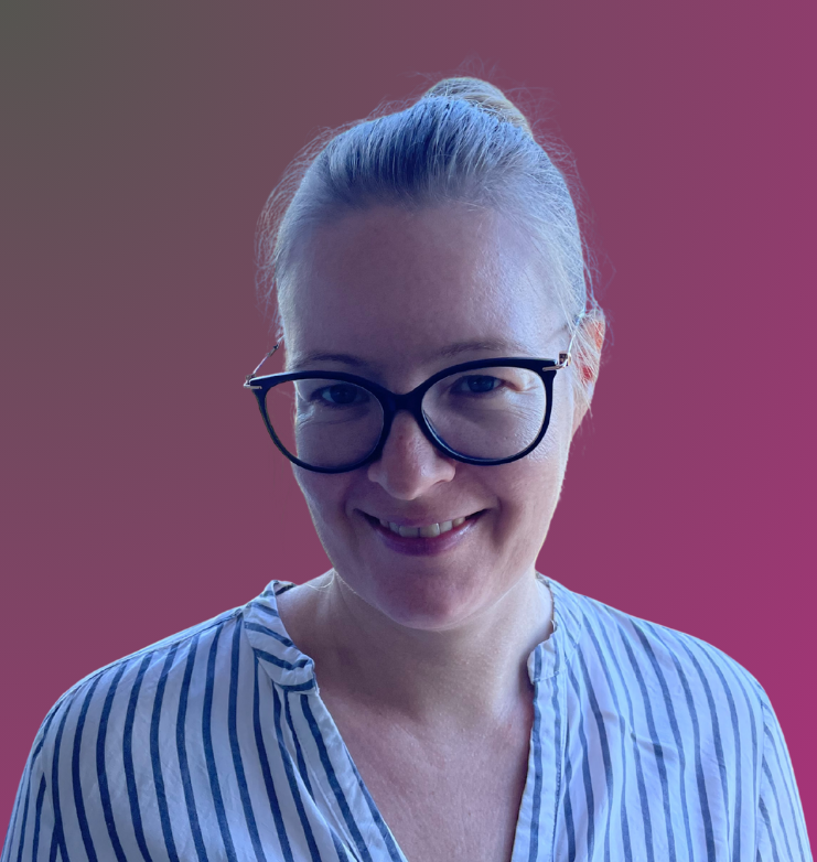 A woman with blonde hair tied back, wearing glasses and a blue and white striped blouse, smiling at the camera against a gradient pink background.