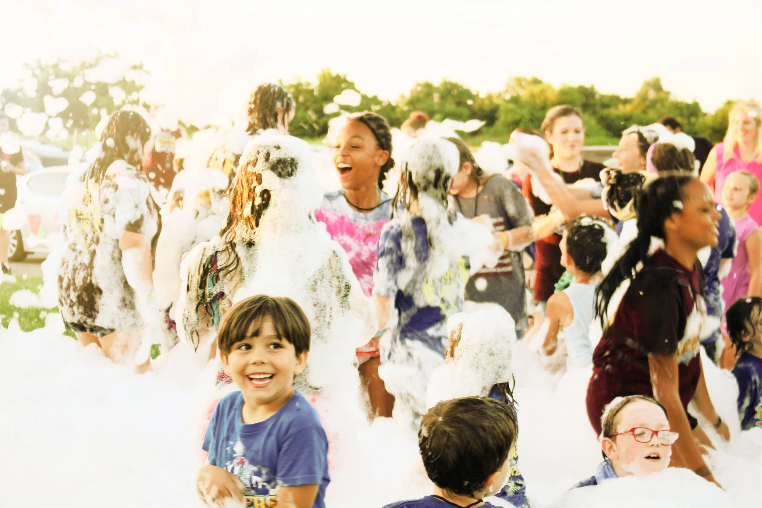Children playing and having fun at a foam or soap event outdoors during daytime.