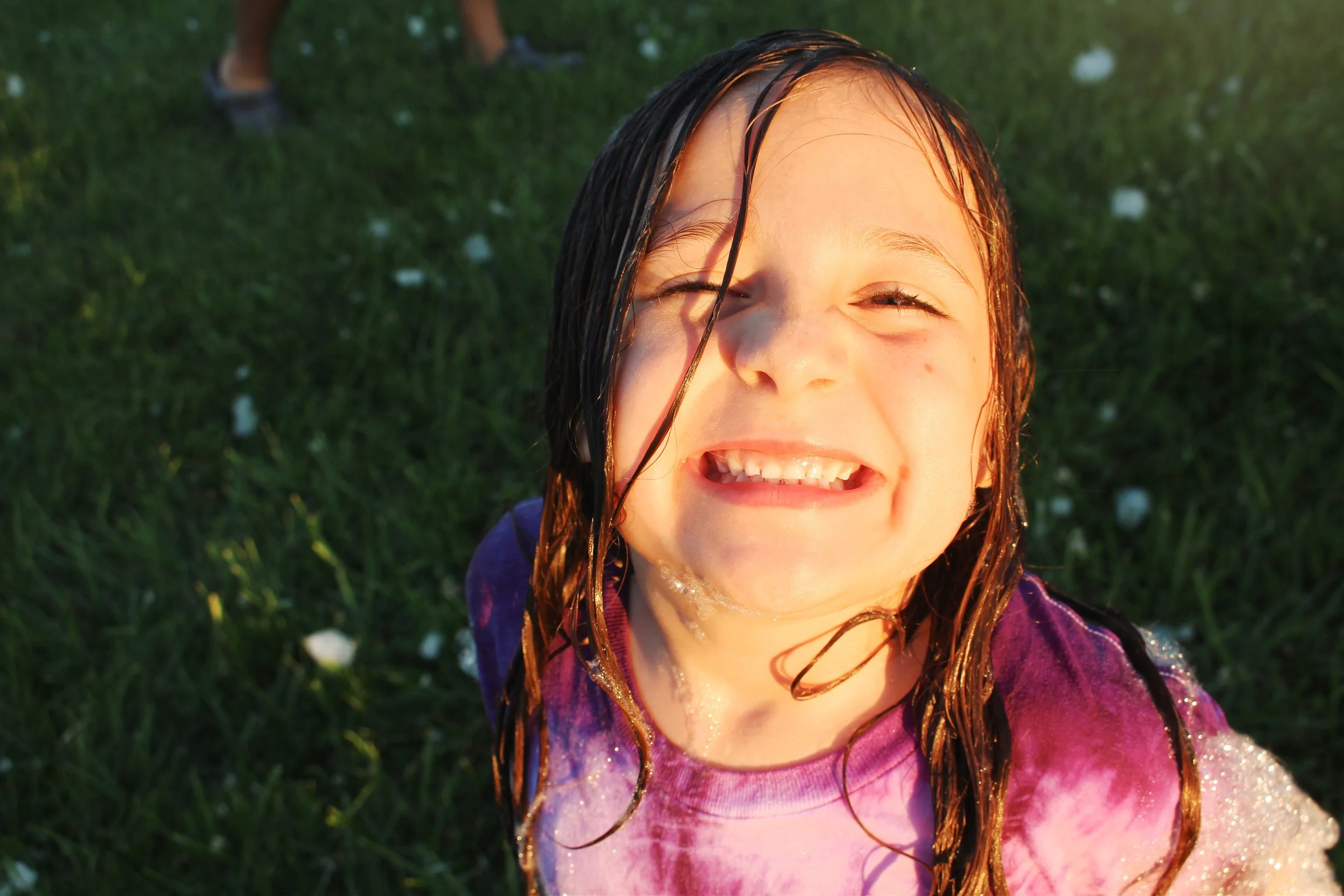 A young girl with wet hair smiling outdoors on a grassy field.