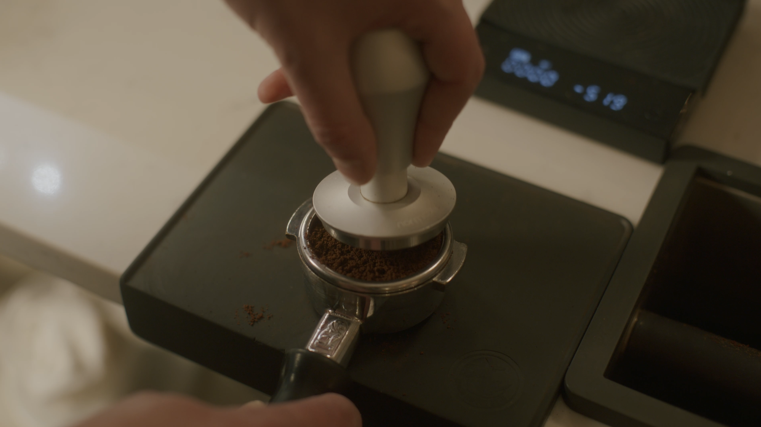 Barista pressing a tamper on ground coffee in a portafilter on an espresso machine at Wisconsin coffee shop.
