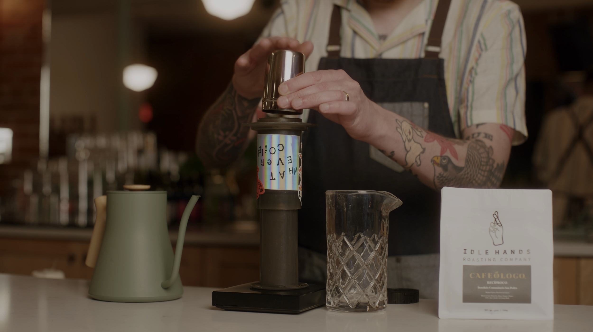 Coffee enthusiast with tattooed arms pouring coffee grounds into an aeropress to brew coffee at a midwest coffee shop.