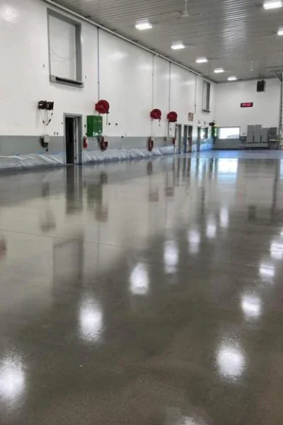 Empty industrial or warehouse space with a polished concrete floor, white walls, red fire equipment, and high ceiling with fluorescent lighting.