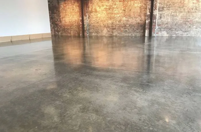 Empty warehouse with polished concrete floor and exposed brick wall in the background.