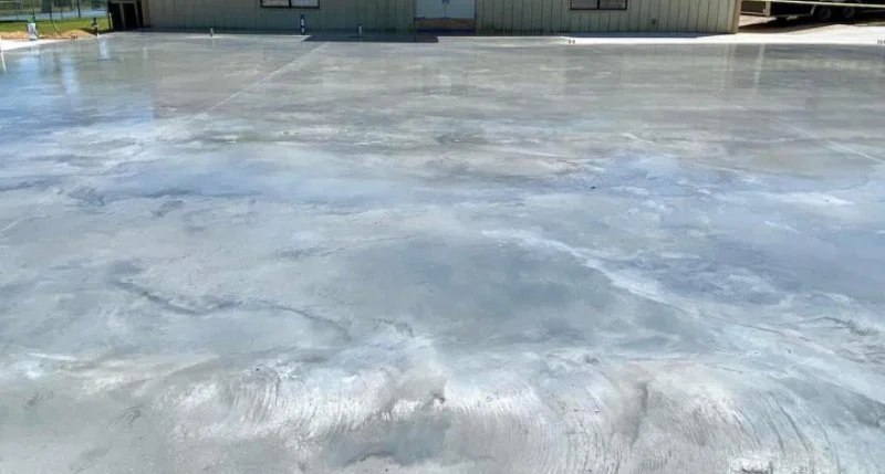 Empty concrete parking lot with a building and fence in the background.