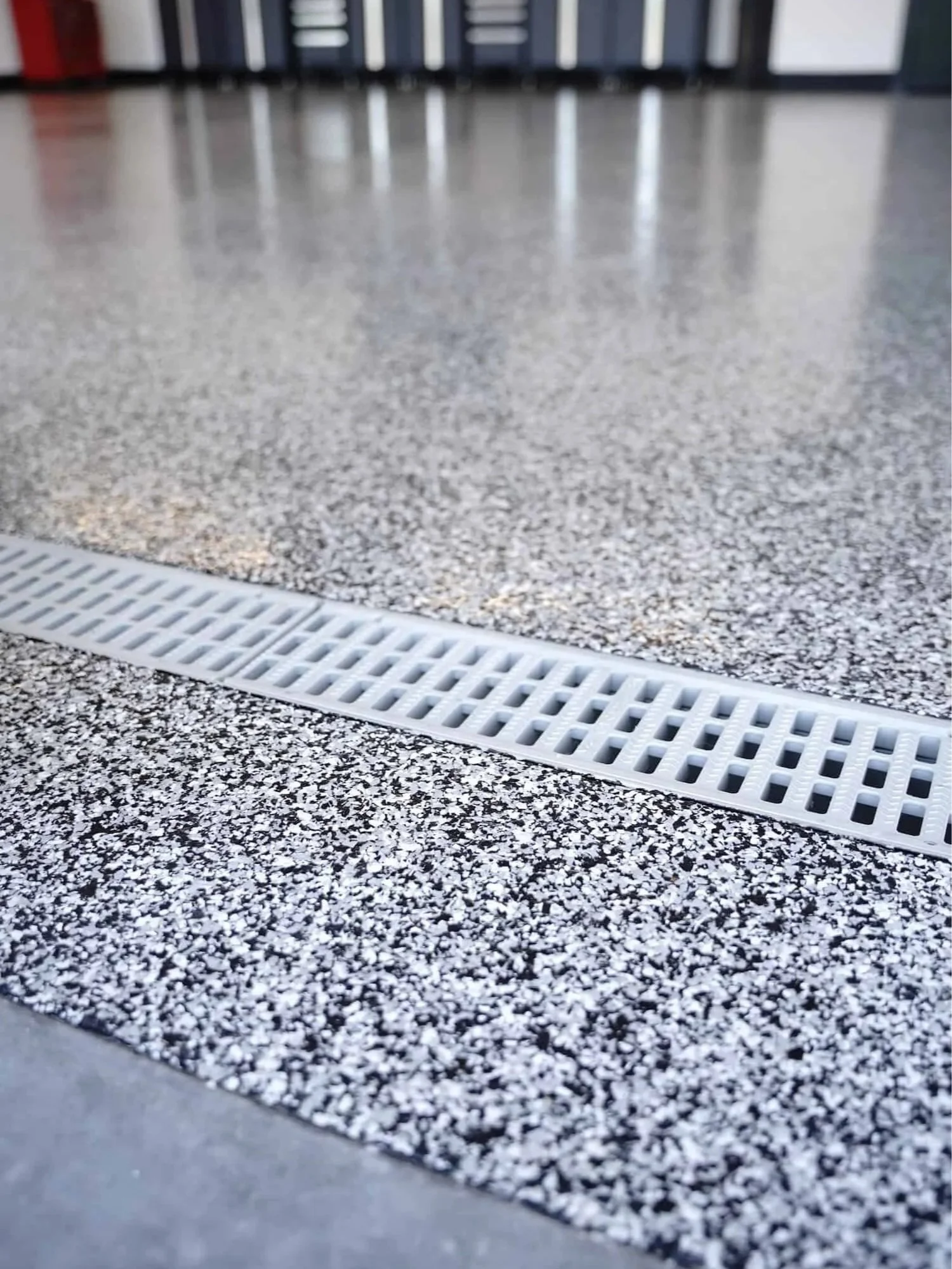 Close-up of a floor drainage grate on a speckled gray floor, with blurred background.