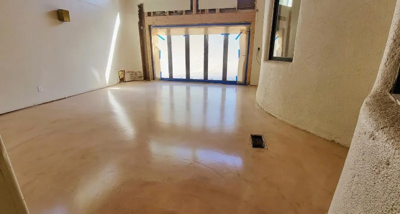 Empty room under construction with a large window covered with blue painter's tape, a curved wall, and a textured wall surface.