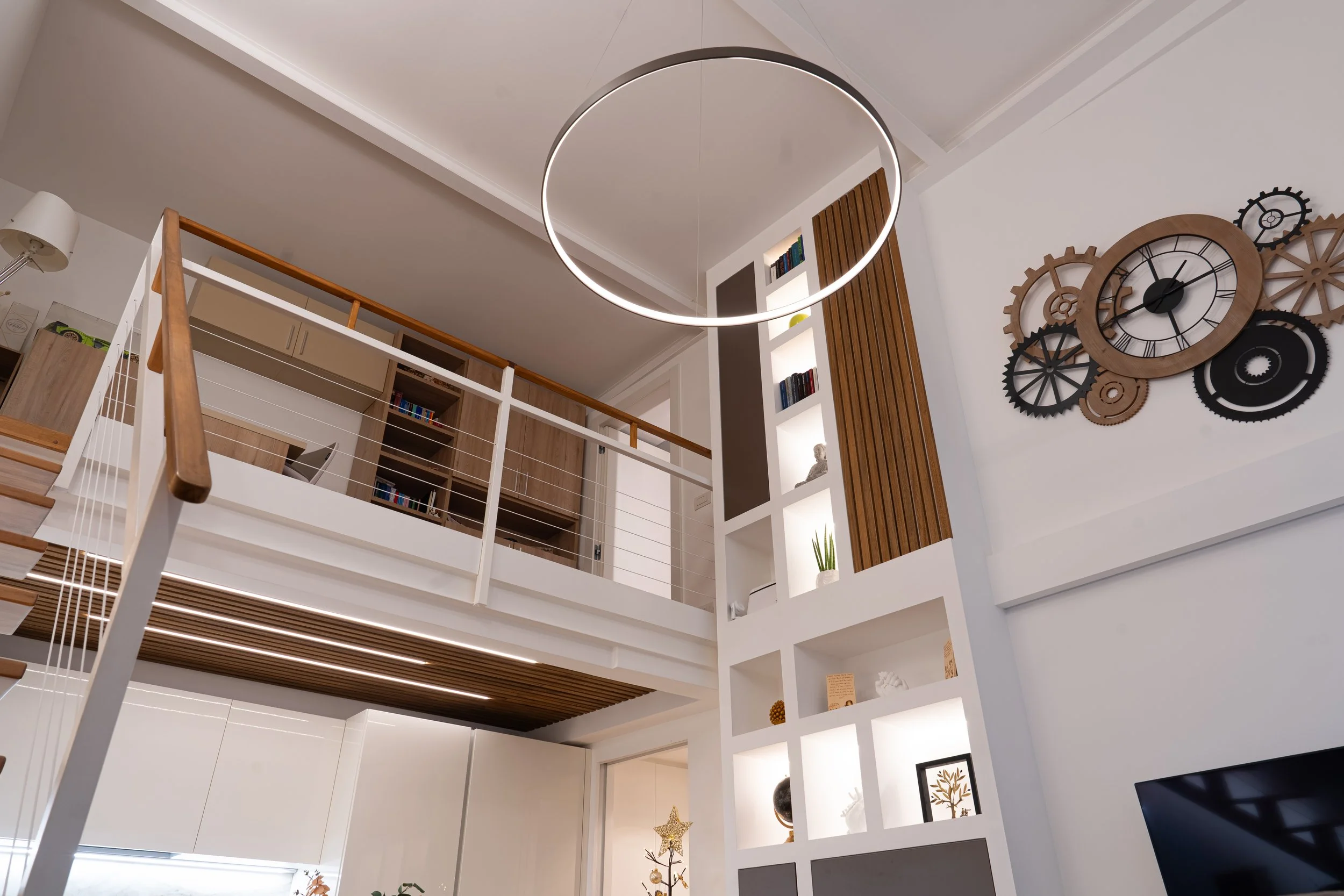 Interno di una casa moderna con soffitto alto, scarpiera e libreria a scomparsa, e un grande orologio a ruota sul muro.