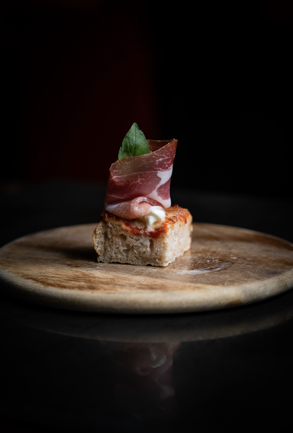 Un antipasto con pane, prosciutto, basilico e formaggio su un tagliere di legno.