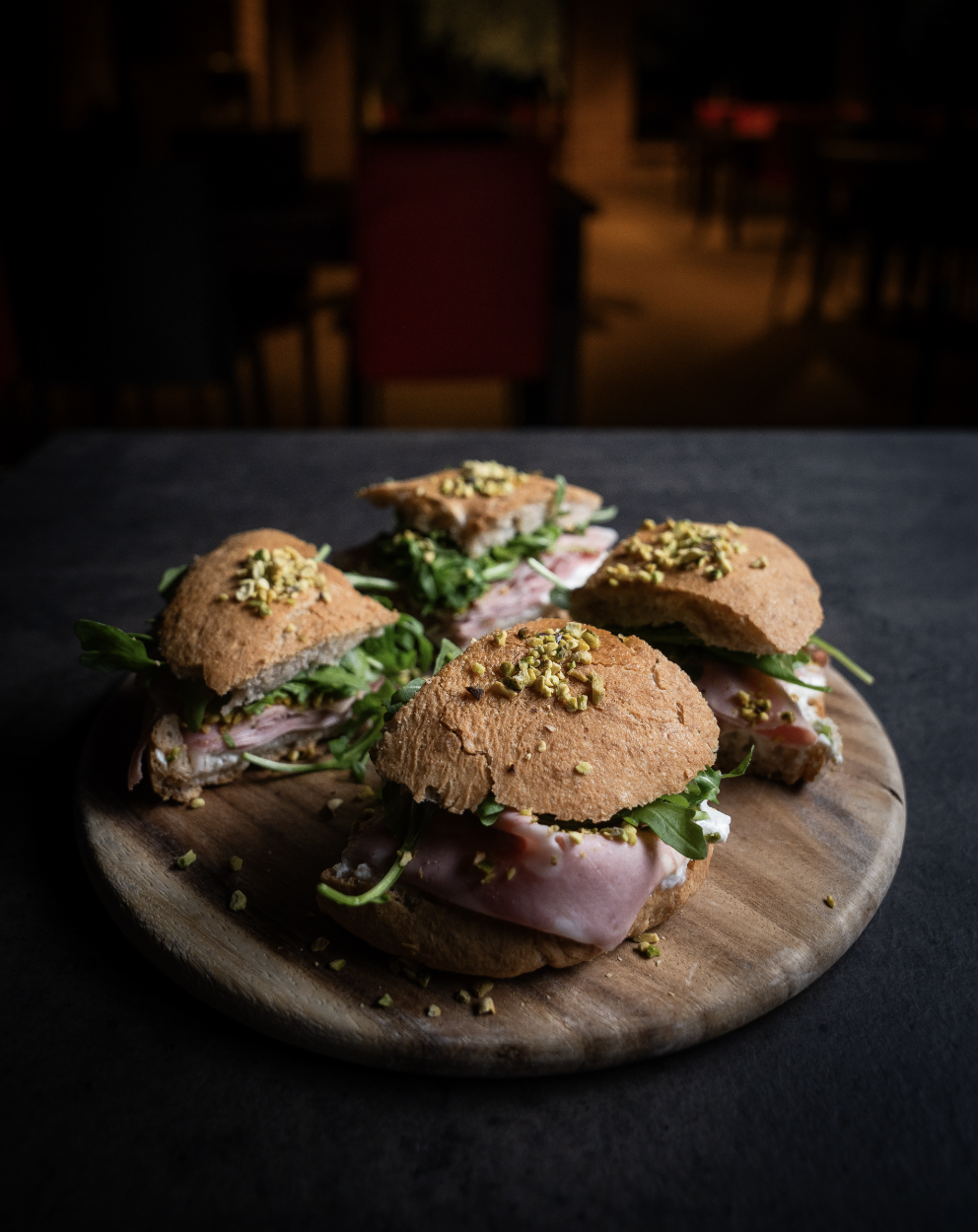 Panini con prosciutto, rucola e granella di pistacchio su un piatto di legno