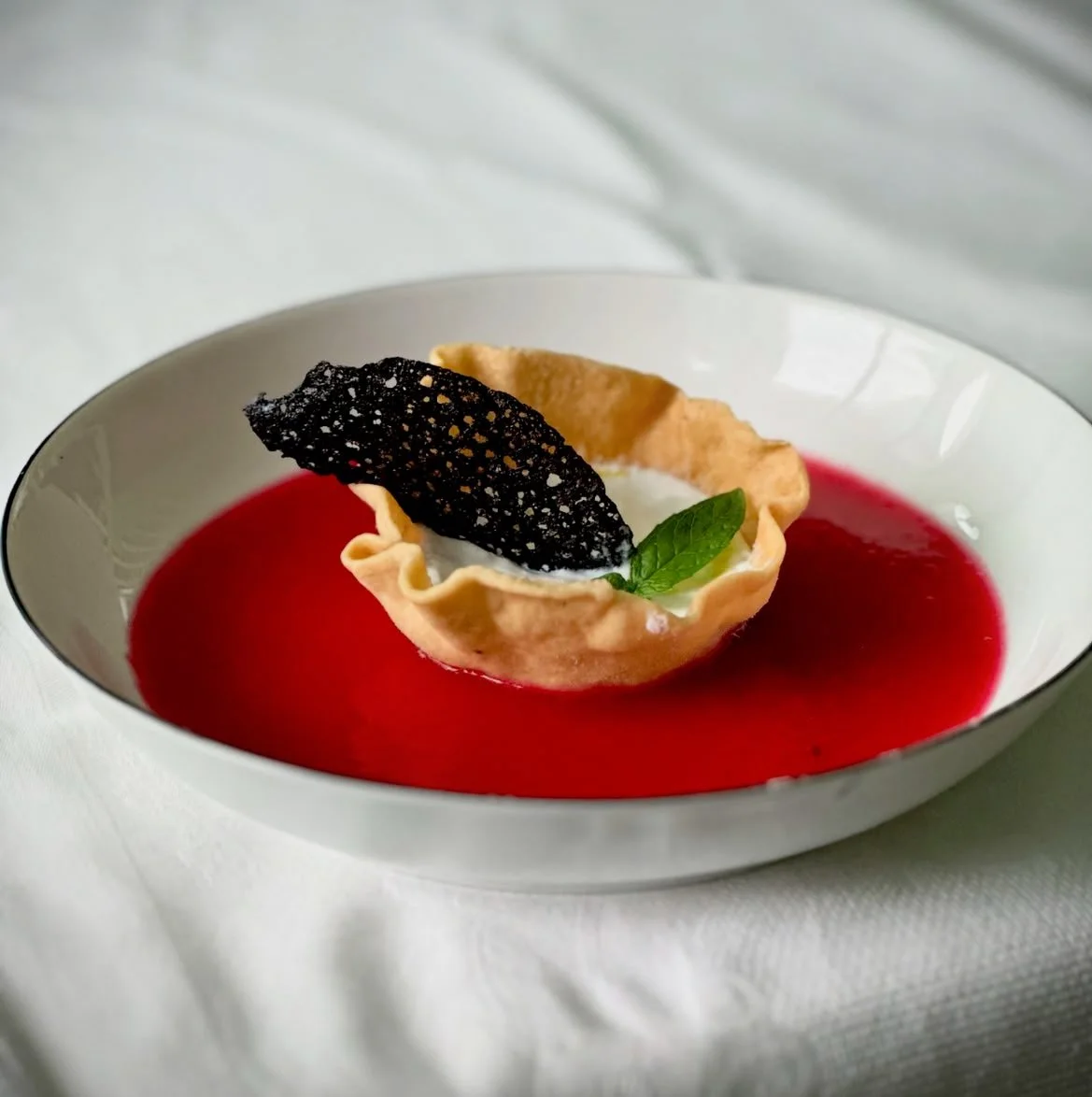 Dolce di frutta con crosta sottile, crema bianca, pesca con foglia di menta e decorazione nera croccante in una ciotola bianca