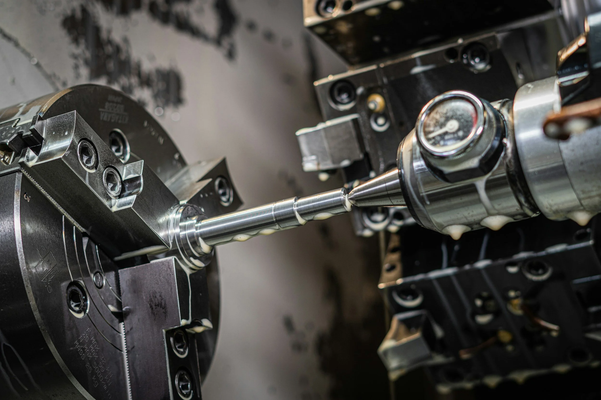 Close-up of industrial machinery with metallic components, including a rotating shaft and a gauge, in a manufacturing or assembly setting.