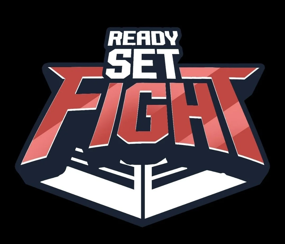 Logo with the words "Ready Set Fight" in bold, stylized letters, with a graphic of a wrestling ring below the text, all on a black background.