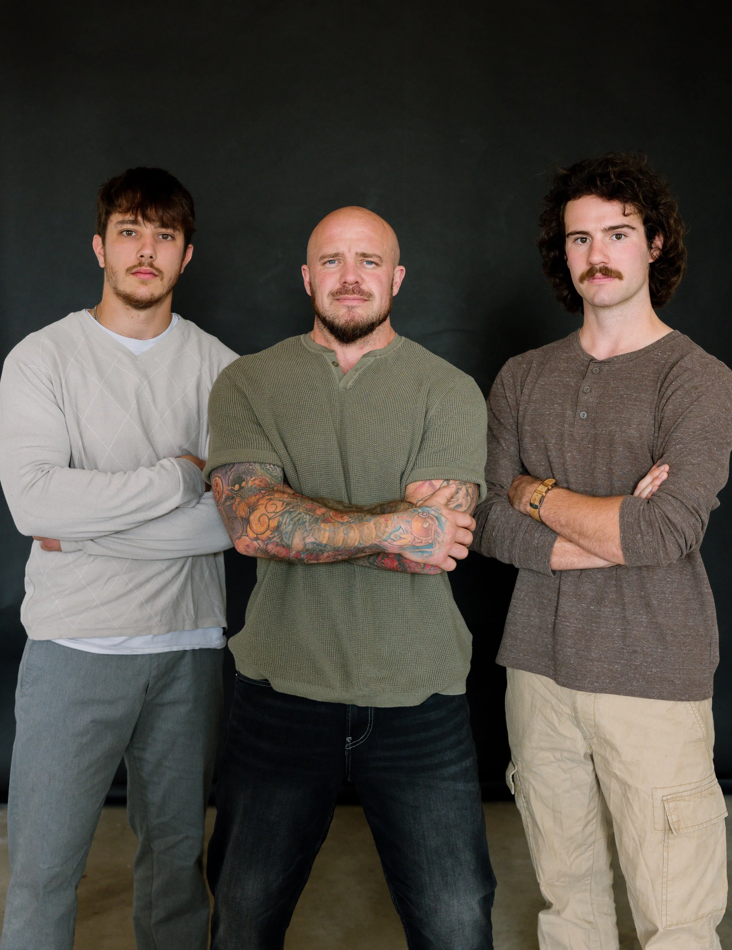 Three men standing with crossed arms in front of a solid black background.