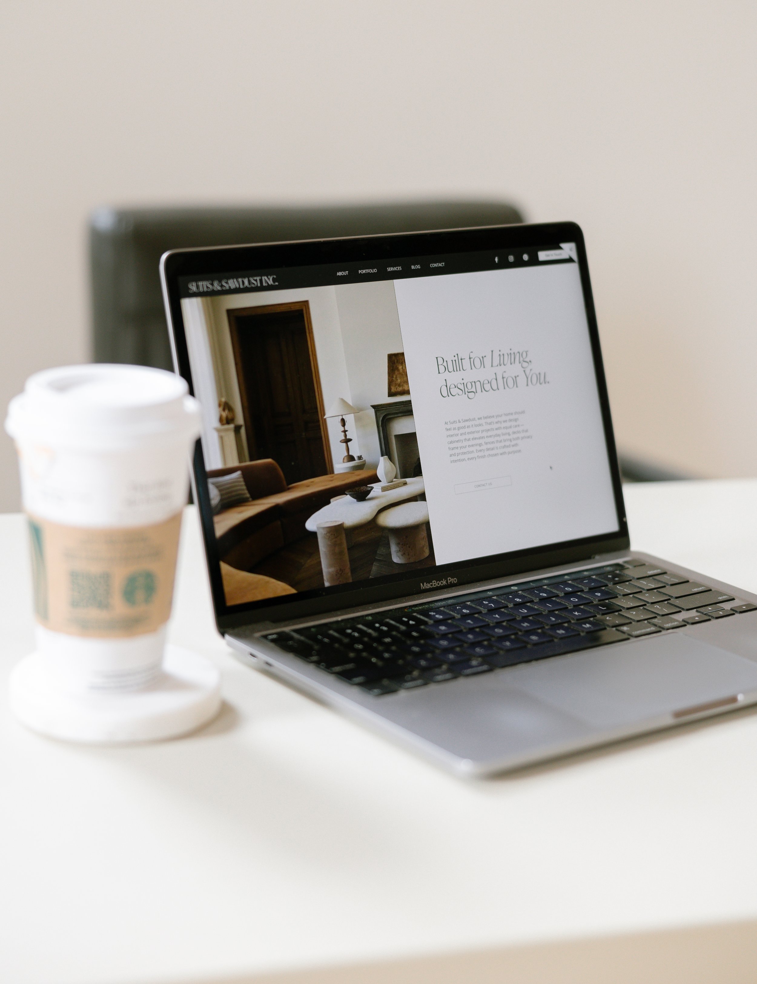 A MacBook Pro laptop displaying a website about interior design, placed on a white desk with a Starbucks coffee cup next to it.