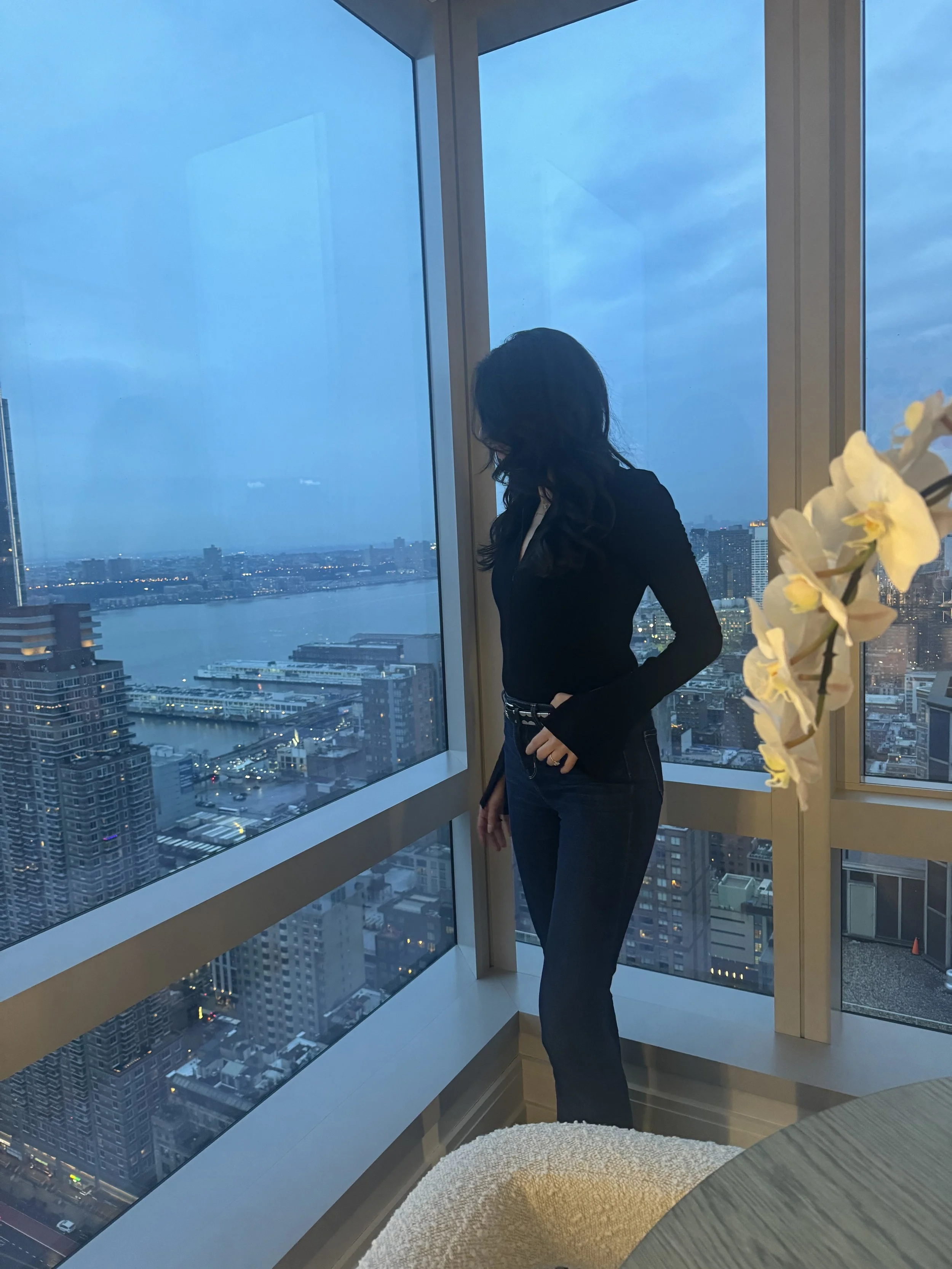 Silhouette of a woman sitting at a desk with a laptop, with her hands on her face, in front of a large window.