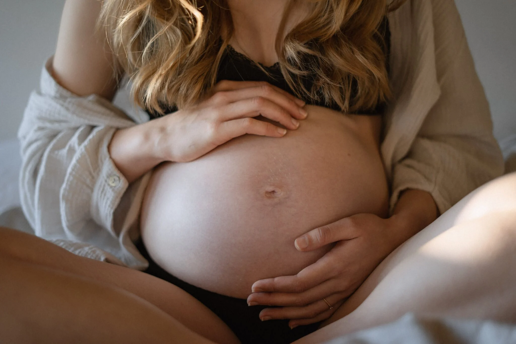 Schwangere Frau läuft auf einem Waldweg und hält ihren Bauch mit beiden Händen, lächelnd.