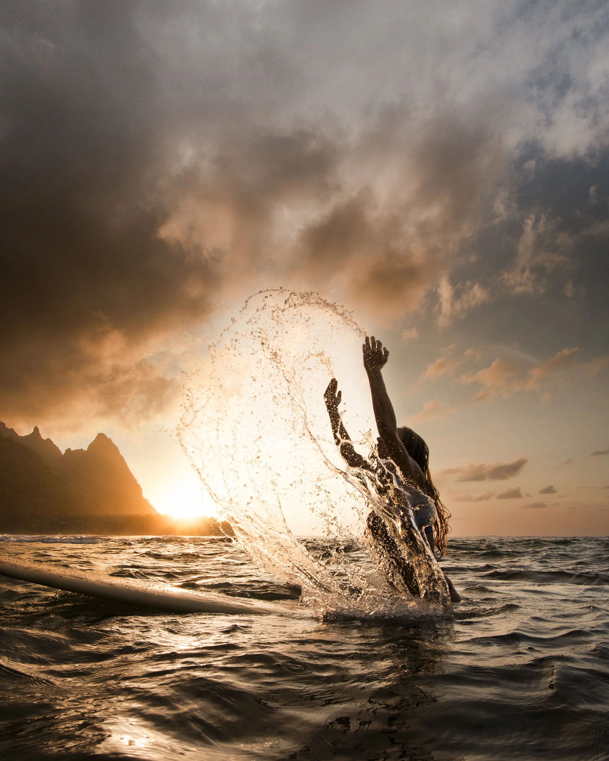 Person splashing water in the ocean at sunset with mountains in the background.