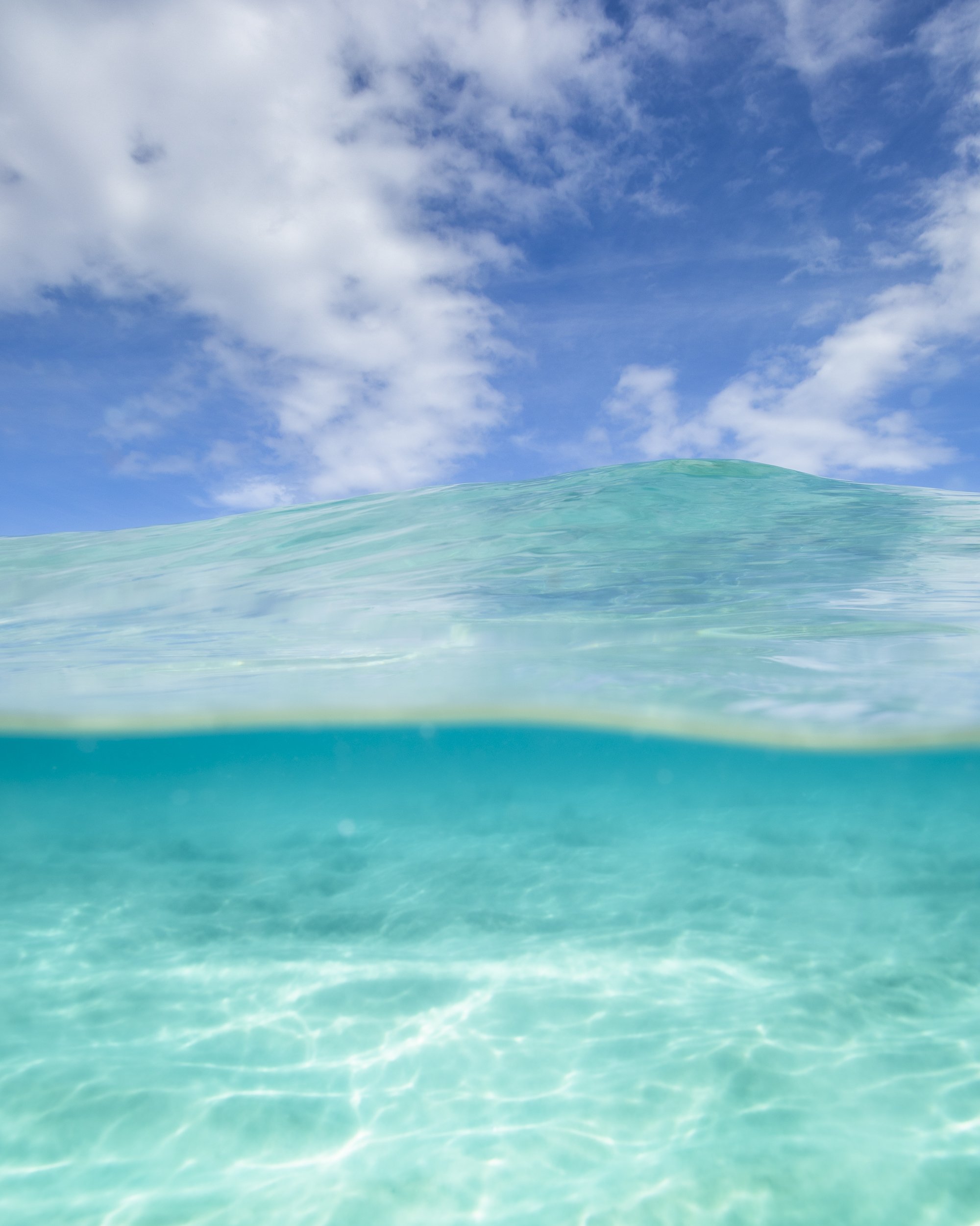 Overhead view of clear turquoise ocean water with a partly cloudy blue sky above.