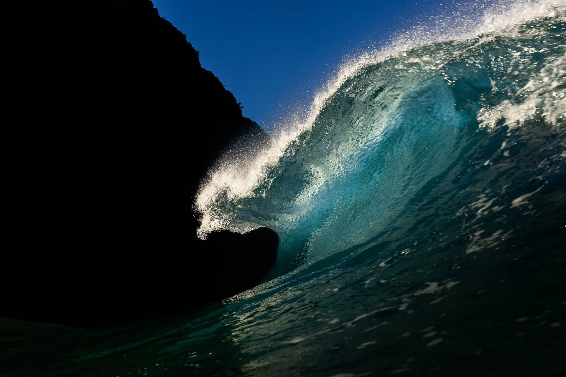 Ocean wave crashing near rocky shoreline on a clear day