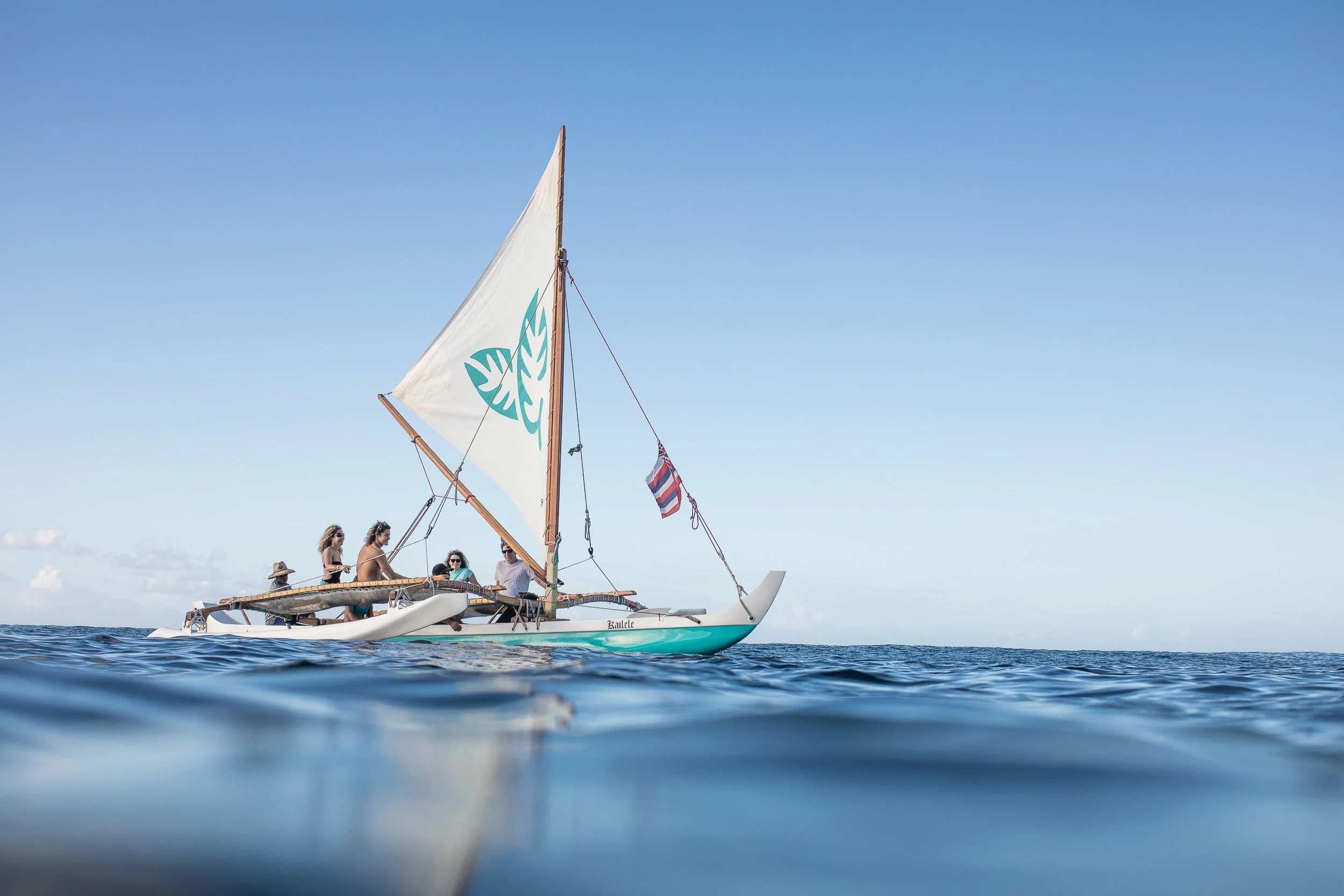 A sailboat with five people aboard floating on the ocean under a clear blue sky.