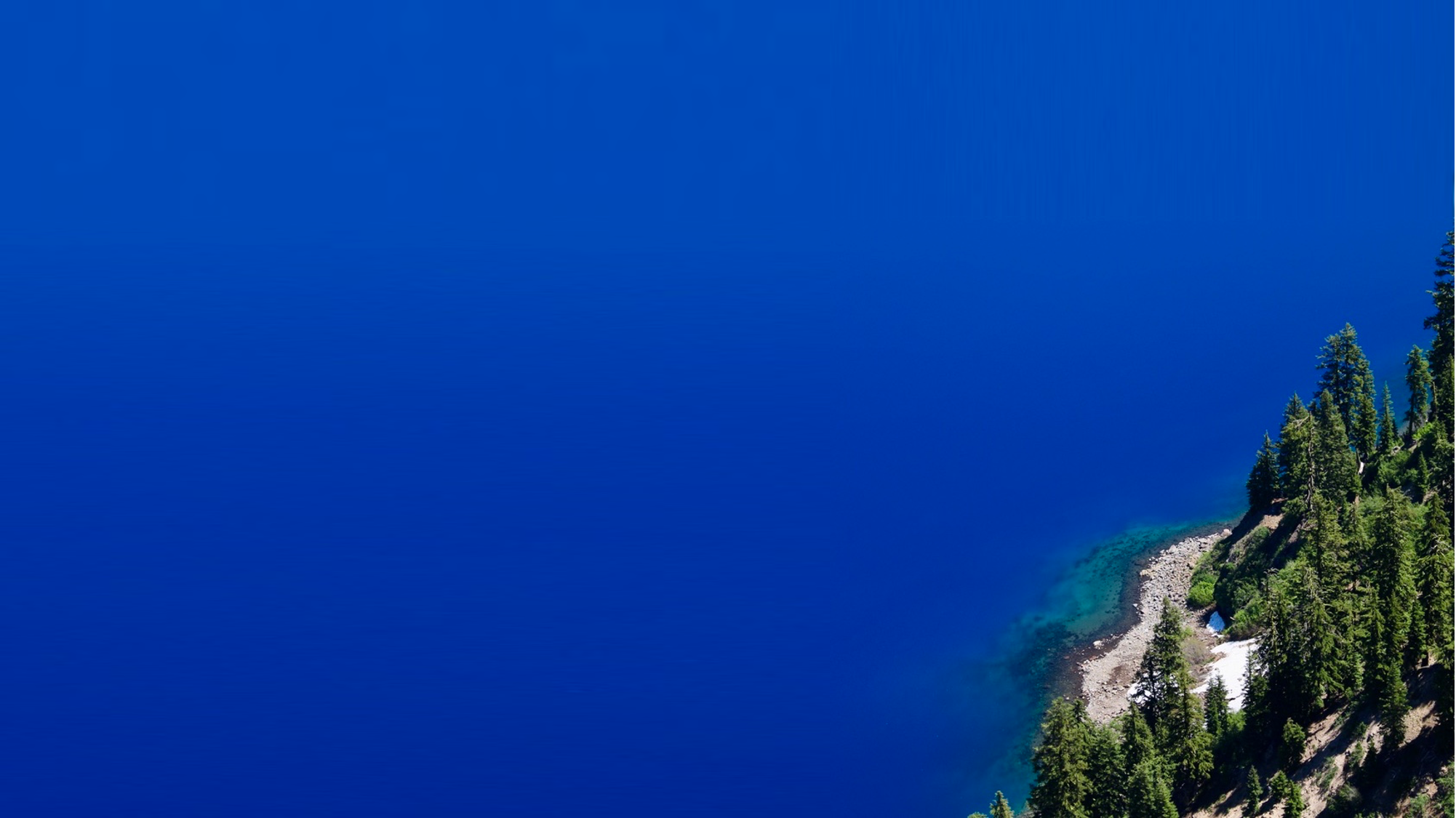 Aerial view of a lake with deep blue water and a forested shoreline on the right side.