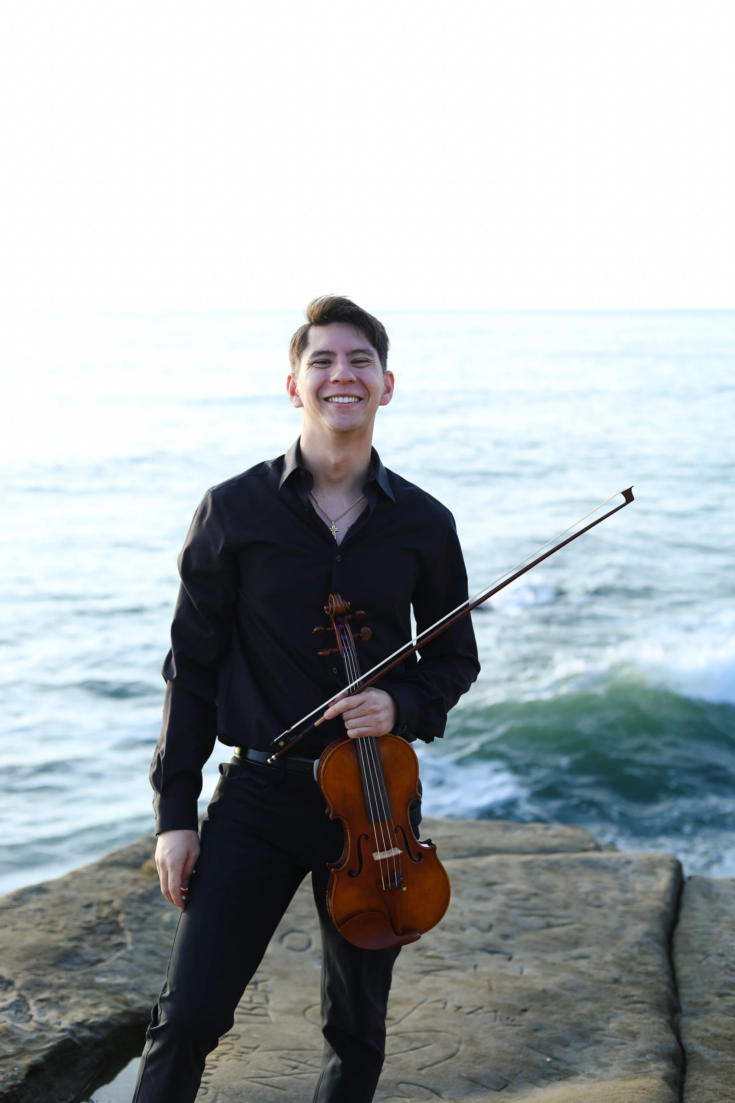Adrian smiling with his violin at the beach