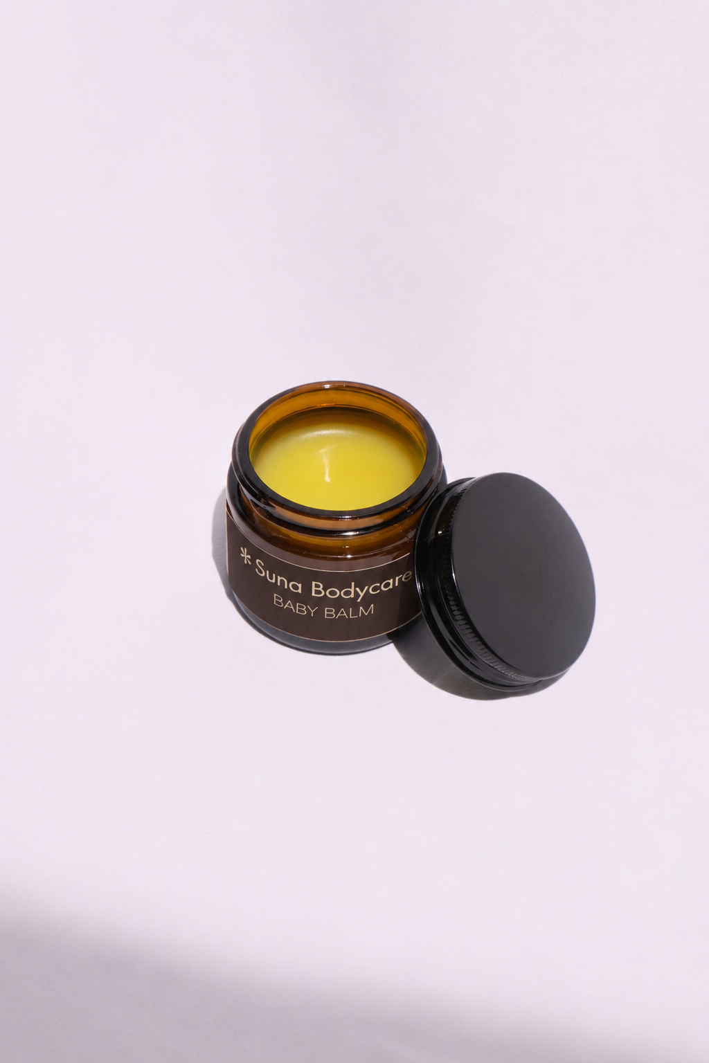Three containers of Suna Bodycare Baby Balm, two small jars and one larger jar, placed on a white surface against a white background.