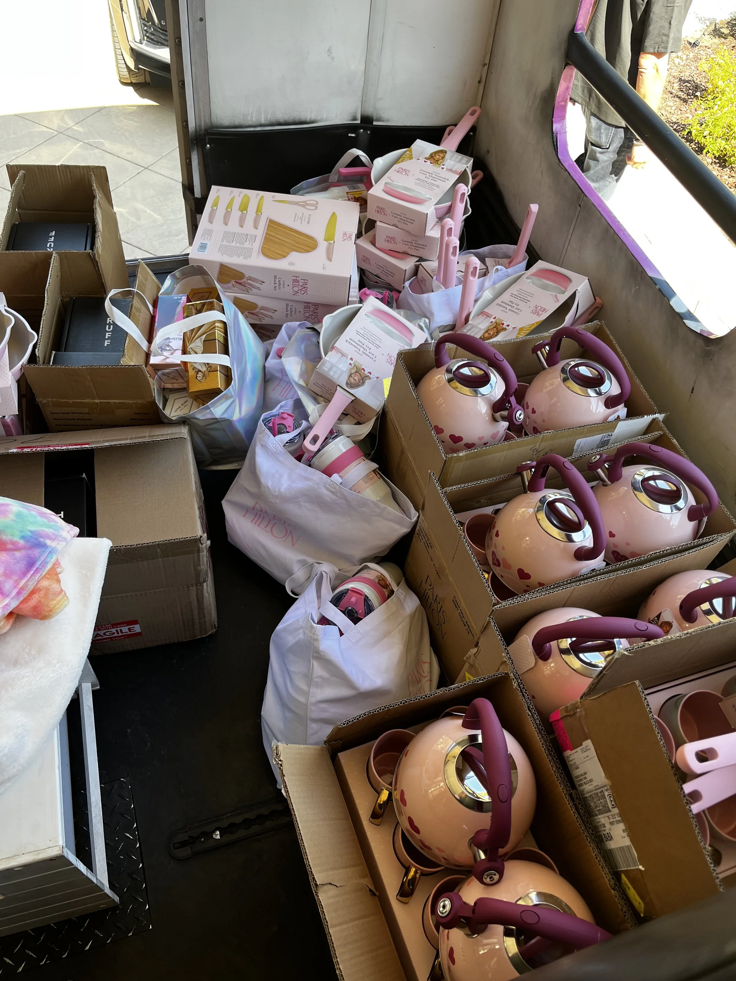 Several pink and black unicorn-themed kettles and kitchenware items in cardboard boxes, with some boxes and bags holding pink kitchen utensils and accessories.