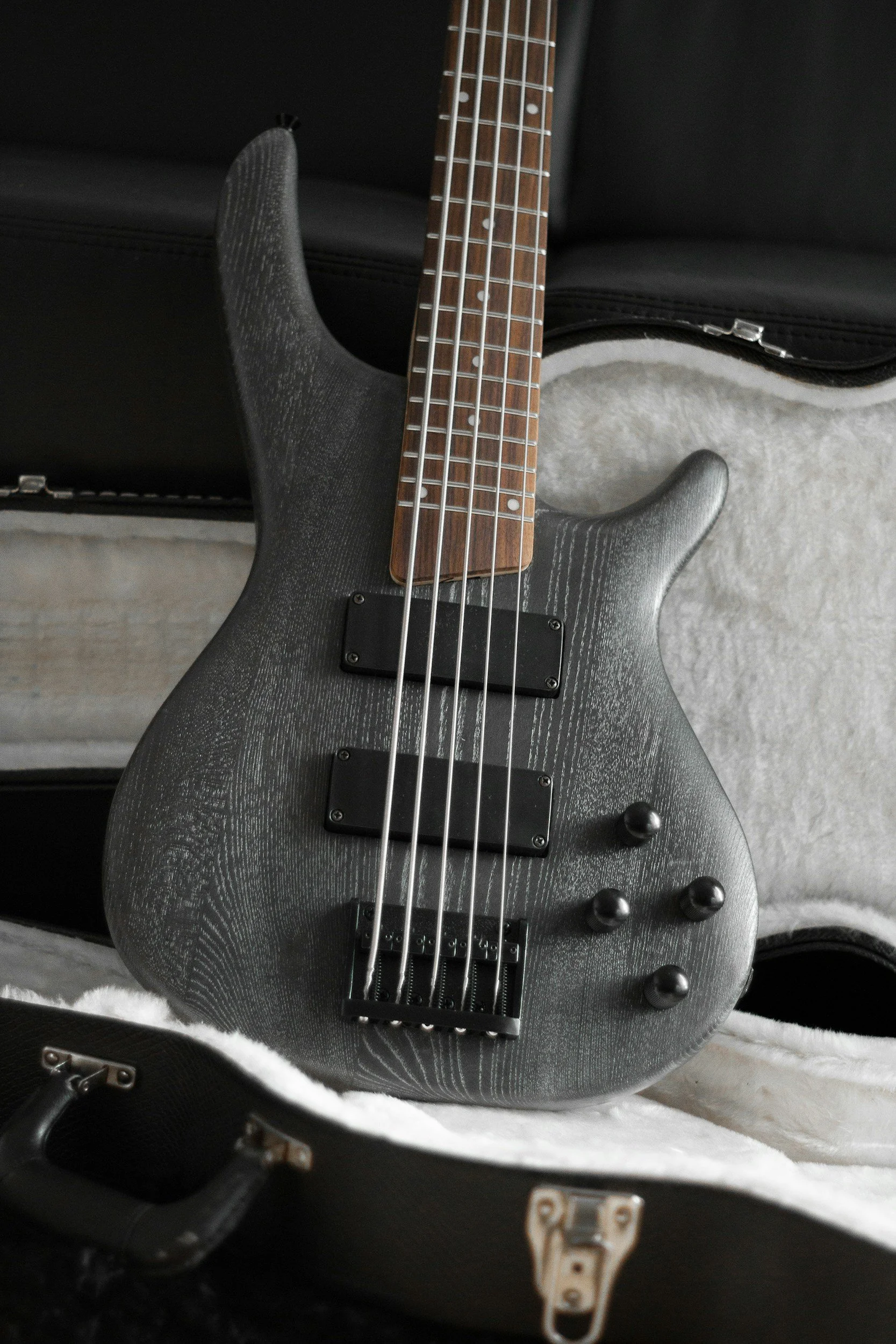 Guitarra eléctrica de color gris oscuro con acabado de madera visible y manijas negras, descansando en una funda con interior de felpa blanca.