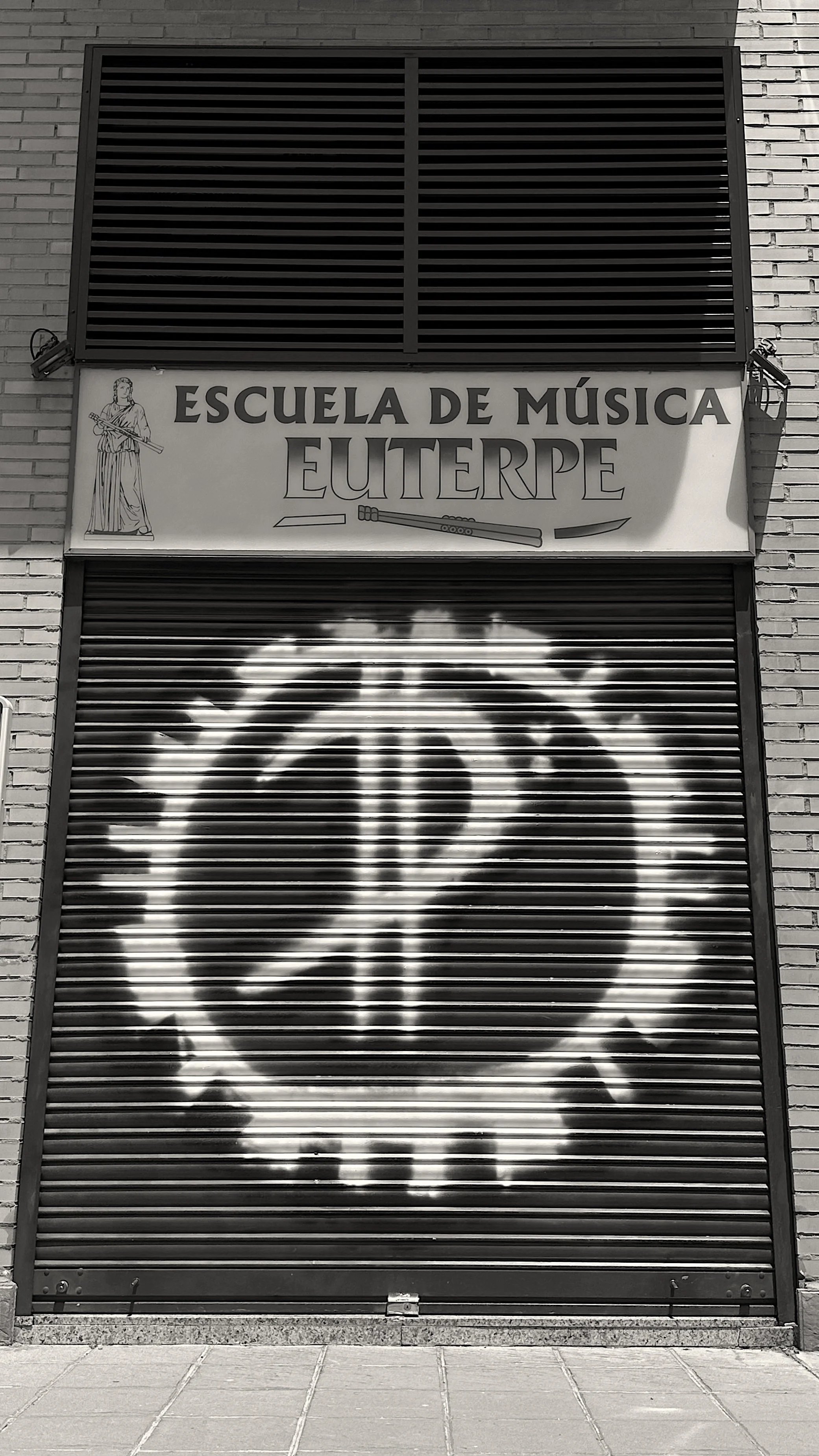 Una puerta metálica enrollable con un graffiti de la cara de un hombre con barba y bigote, en un ambiente urbano.